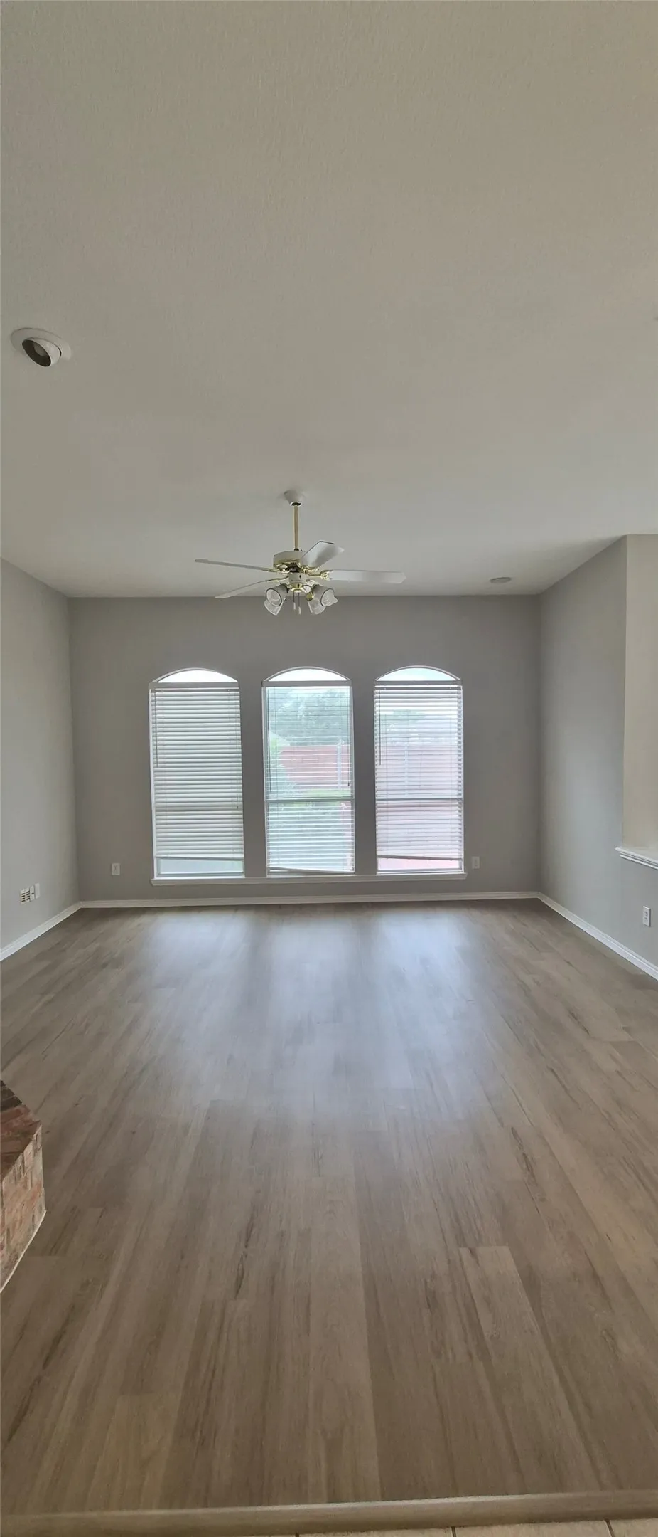 Spacious area featuring wood-finish flooring, three arched windows with blinds, a ceiling fan with light fixture, and recessed lighting