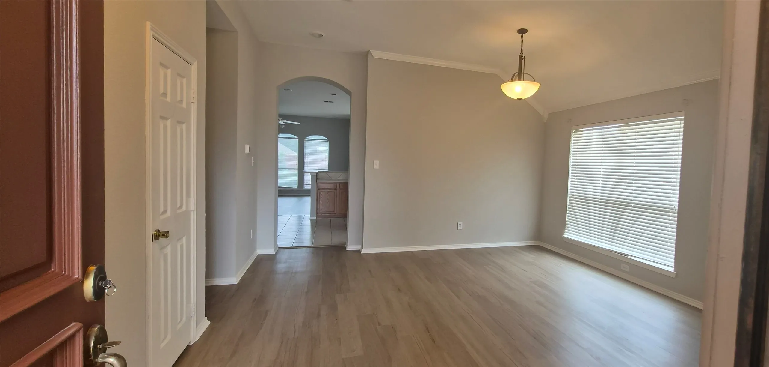 Wood-finish flooring, vaulted ceiling, crown molding, arched entryway, and a hanging light fixture