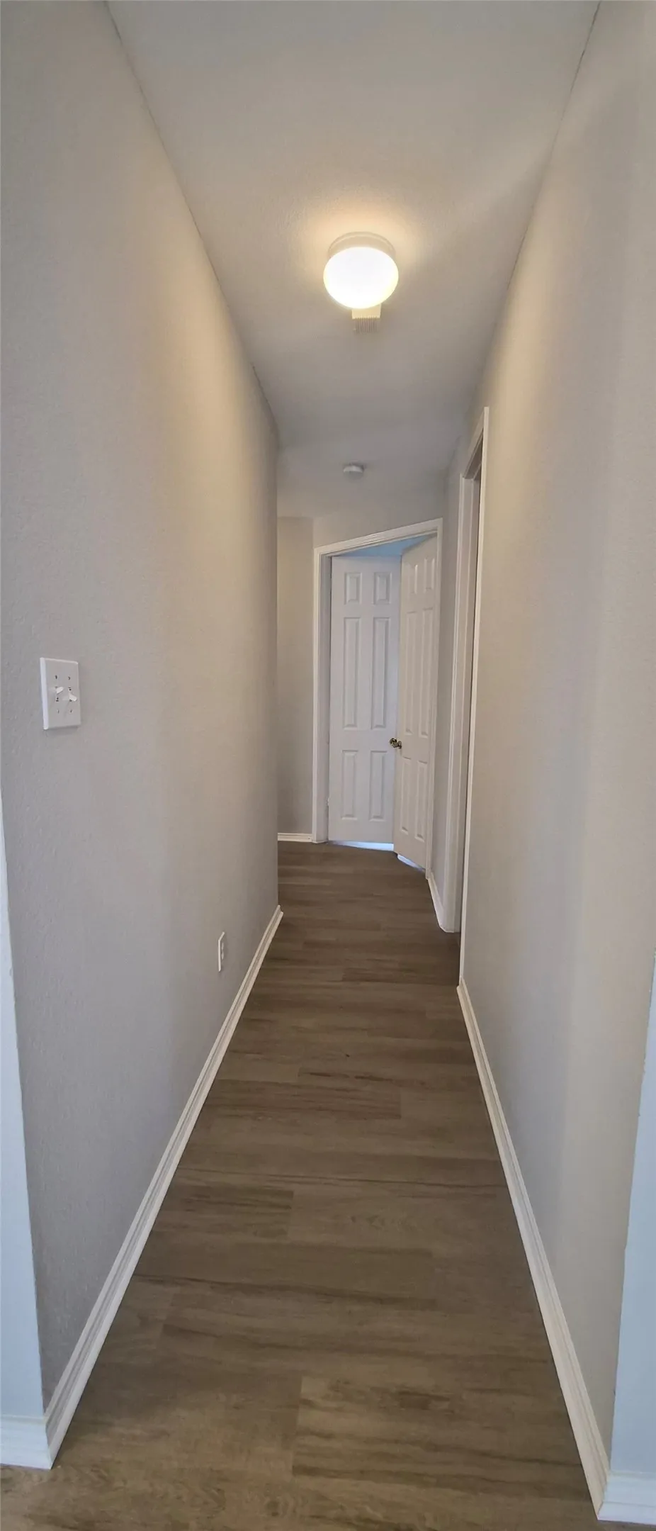 Hallway featuring wood-finish flooring, white baseboards, and a flush-mount ceiling light fixture