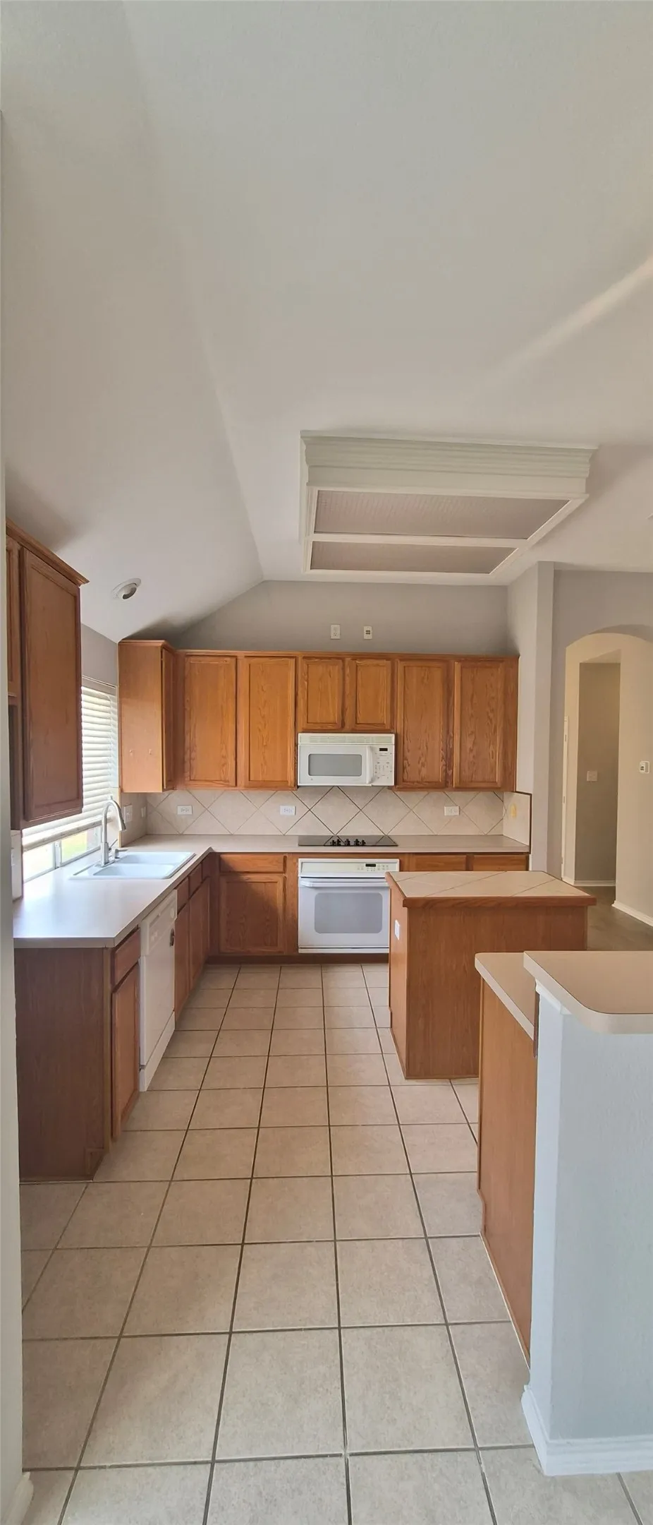 Kitchen featuring wood cabinetry, white appliances, tile flooring, a built-in microwave, and an island
