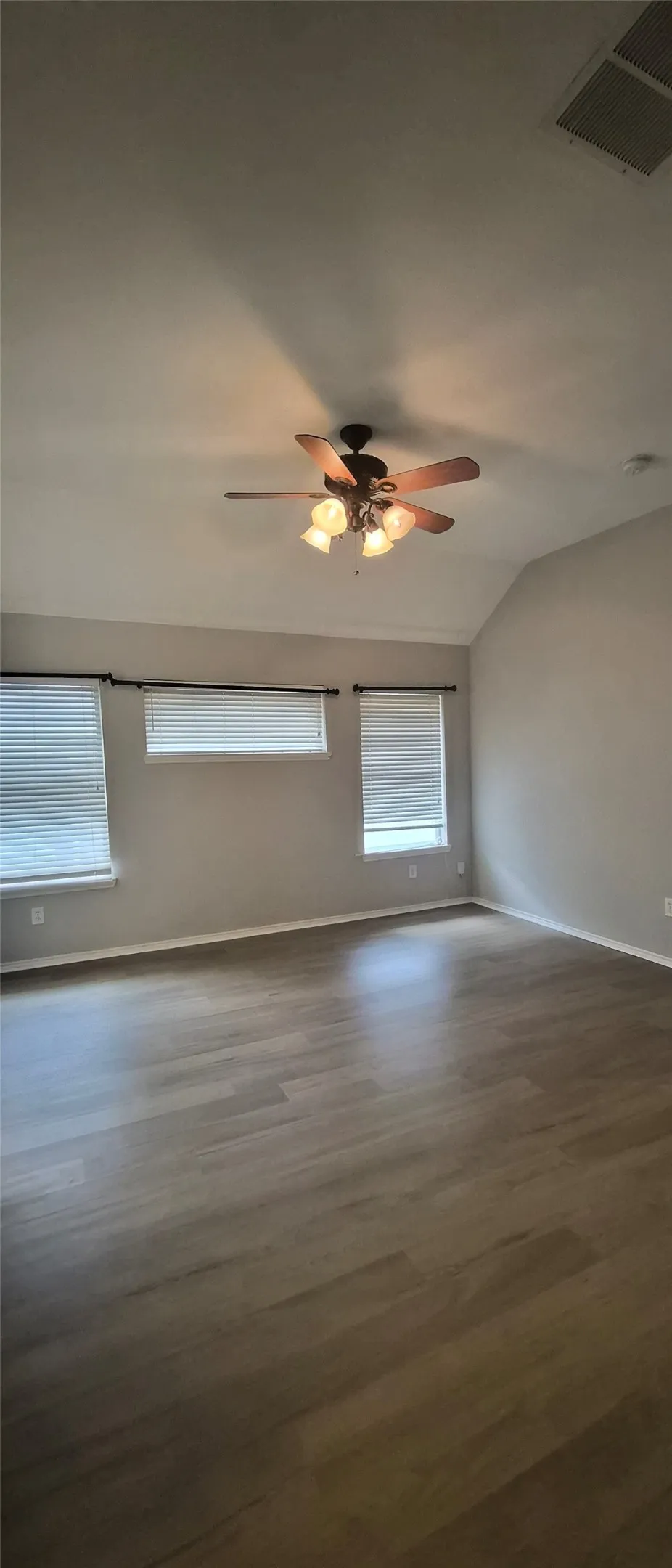 Vaulted ceiling with a four-light ceiling fan, wood-finish flooring, and multiple windows with blinds