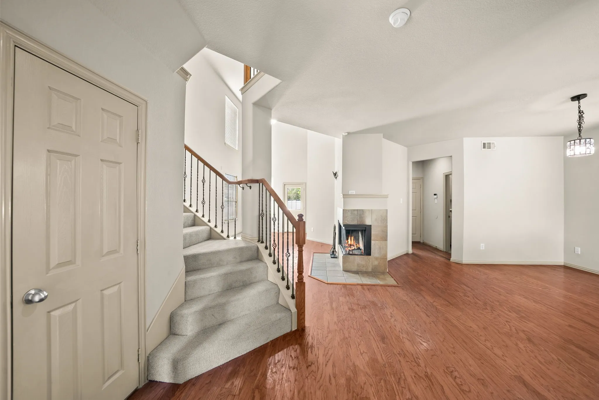 Hardwood flooring, tiled fireplace with hearth, staircase with wrought iron balusters and wood handrail, and a contemporary chandelier