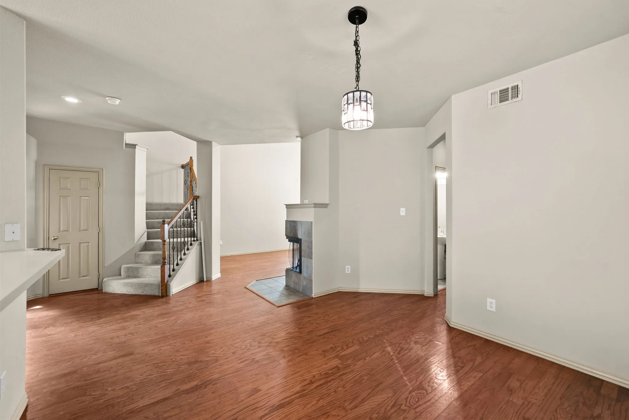 Hardwood-style flooring throughout, modern chandelier, built-in fireplace with tile surround, carpeted staircase with wood banister, and an open concept layout