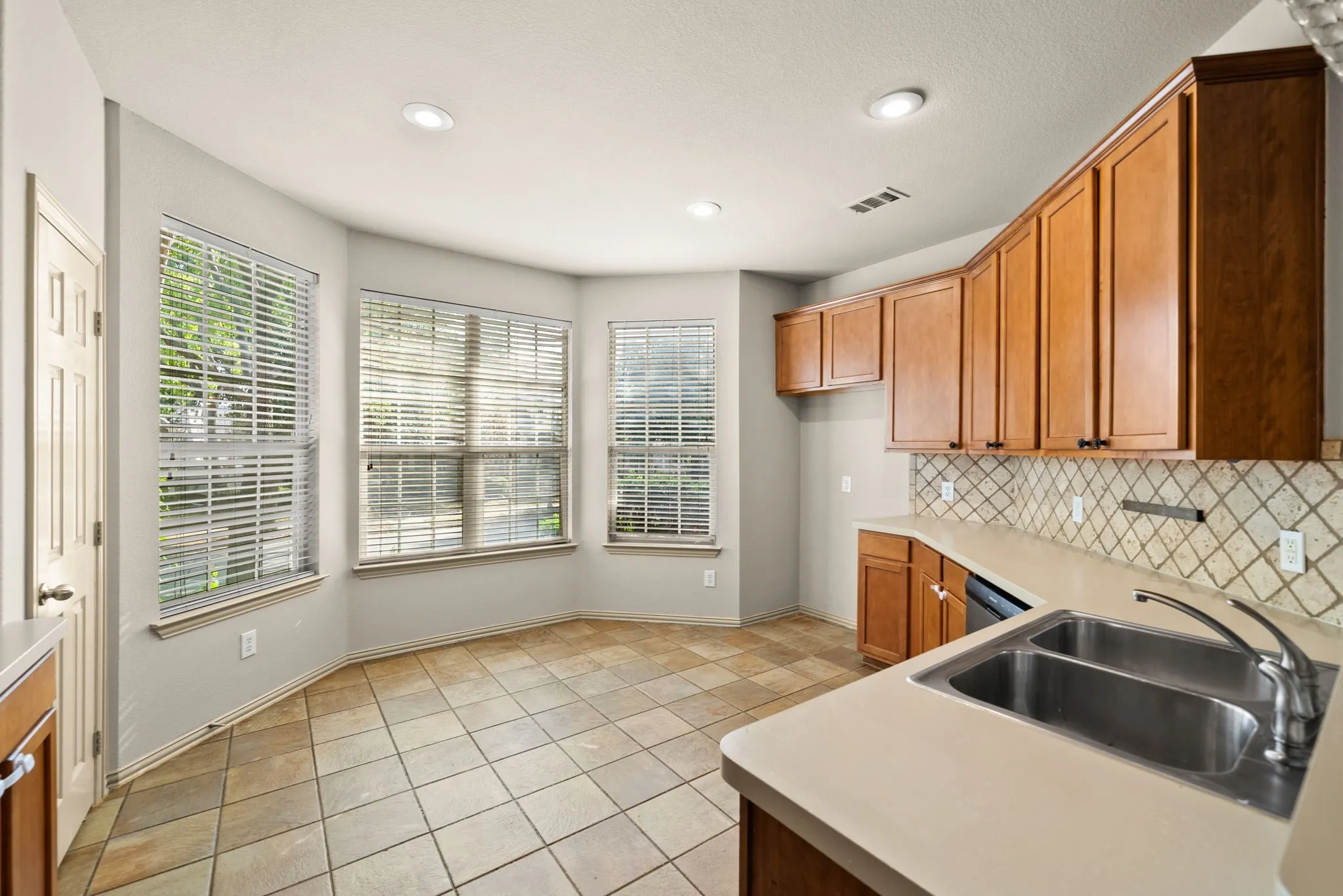 Kitchen featuring wood cabinetry, solid surface countertops, a double basin stainless steel sink, tile flooring, and recessed lighting