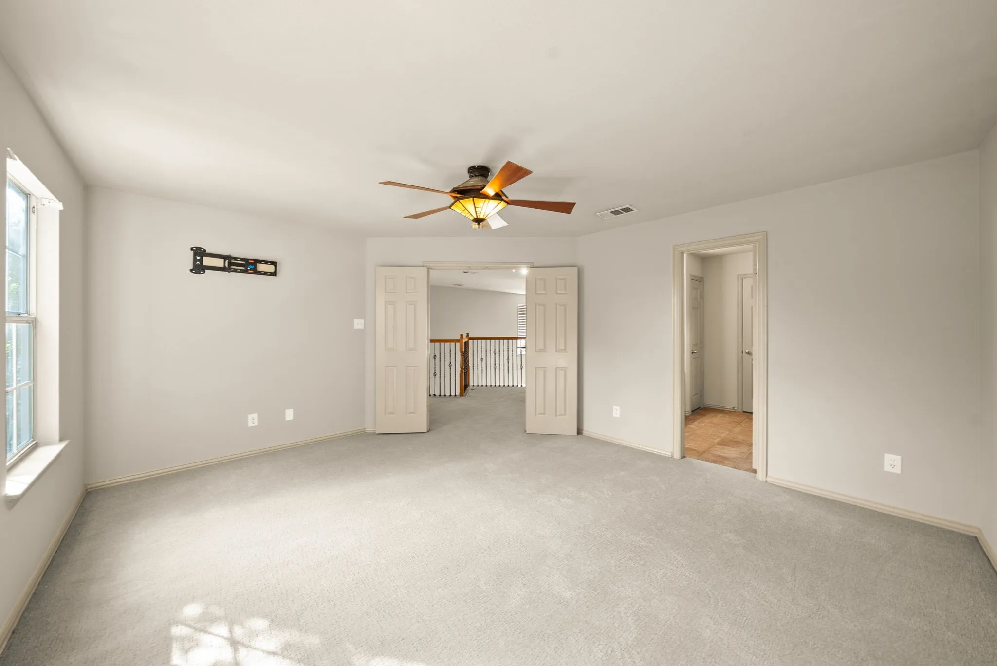 Spacious interior with neutral-toned walls, light-colored carpeting, a ceiling fan with integrated lighting, and multiple windows