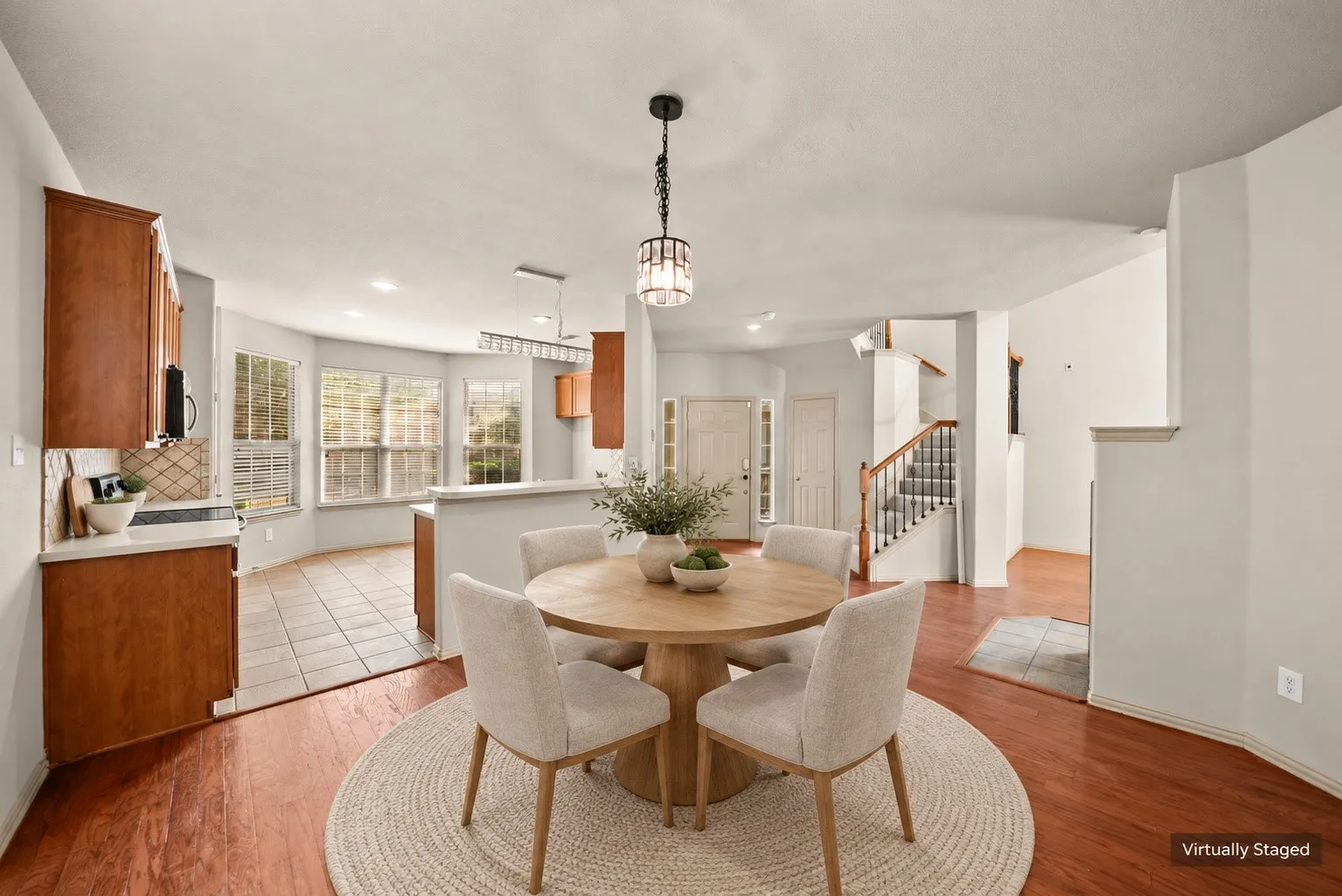Hardwood-finish flooring, staircase with carpeted treads and dark wood newel posts, tile flooring, wood cabinetry, and a multi-pane window bay