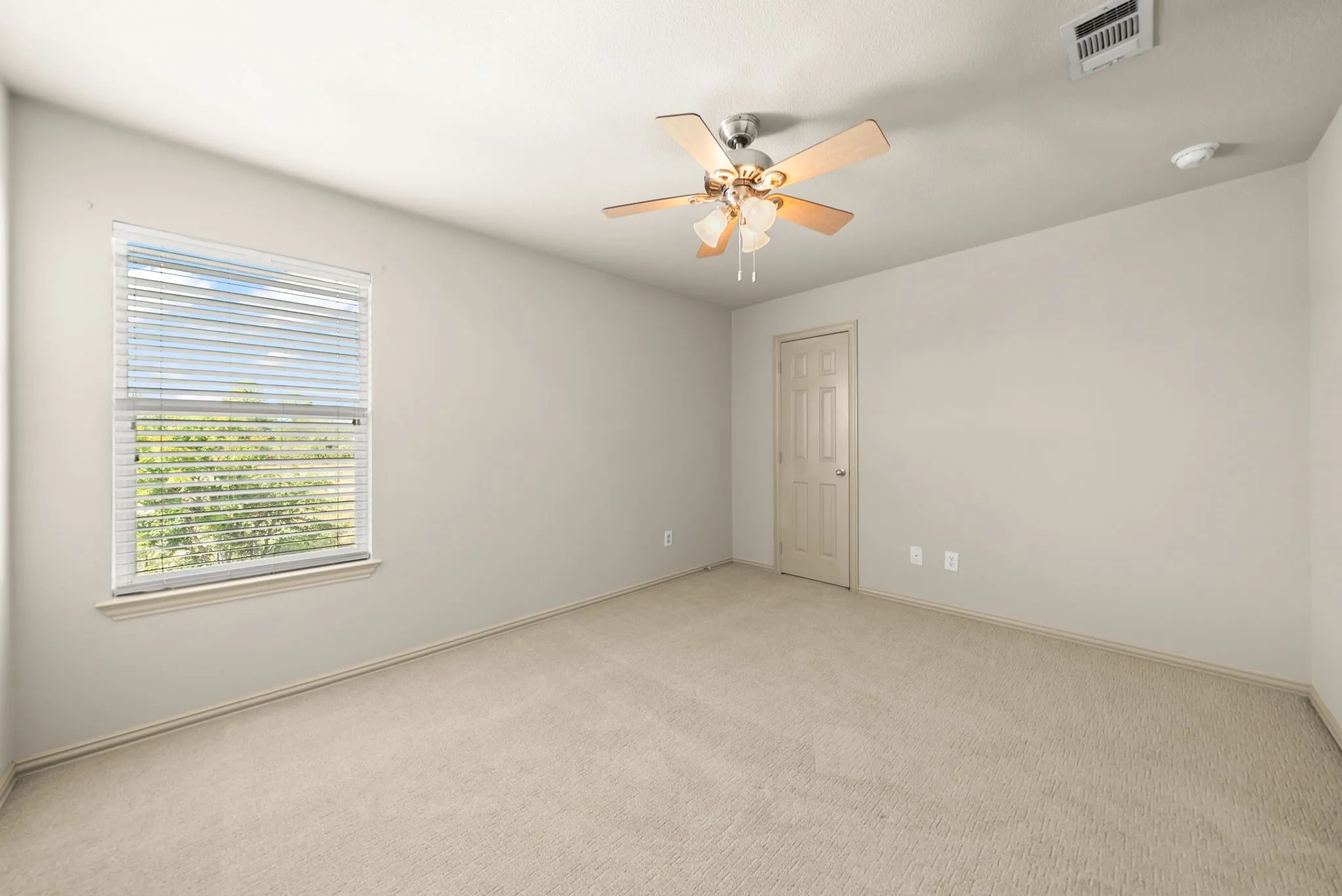 Neutral-toned carpet flooring, light-colored walls, a window with horizontal blinds, a ceiling fan with integrated lighting, and a paneled interior door