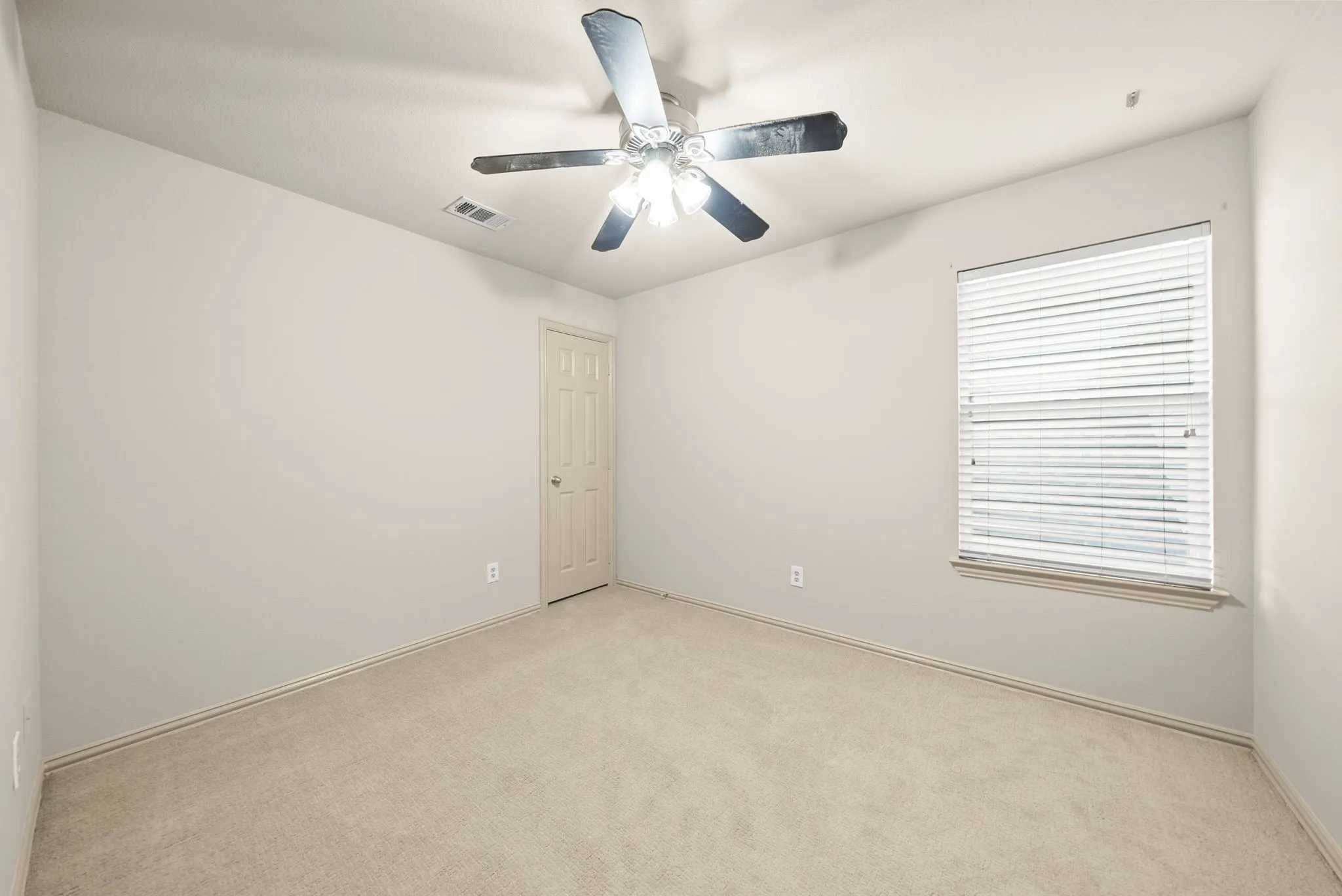 Neutral wall paint, plush carpeting, ceiling fan with integrated lighting, window with horizontal blinds, and a paneled door