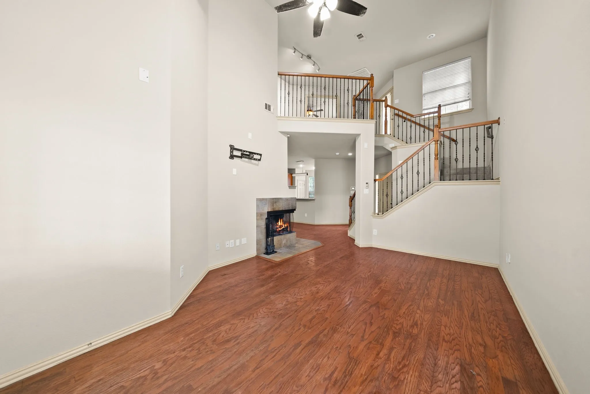 High ceilings, wood-finish flooring, stone-clad fireplace, wrought iron stair railing, and ceiling fan