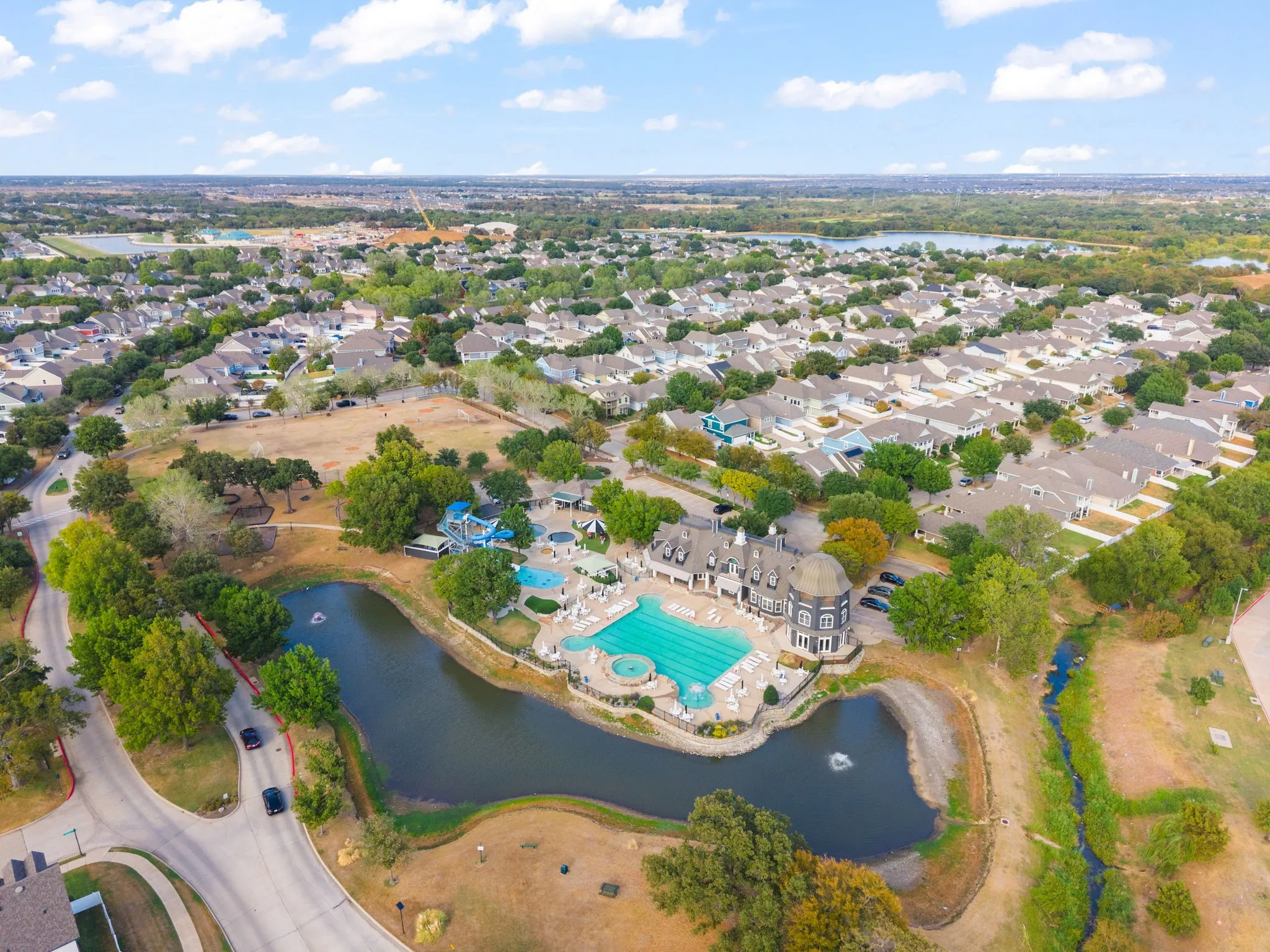 Expansive community featuring a large swimming pool, water park with slides, a community building, and a serene pond with a water feature