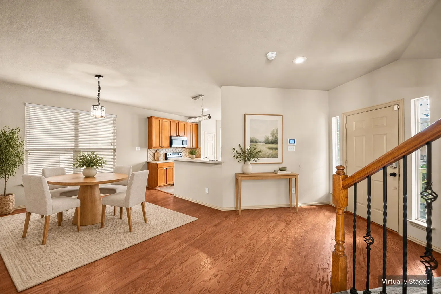 Wood-finish flooring throughout, kitchen with wood cabinetry and stainless steel appliances, dining area with a contemporary chandelier, and a staircase featuring a wood banister with wrought iron spindles