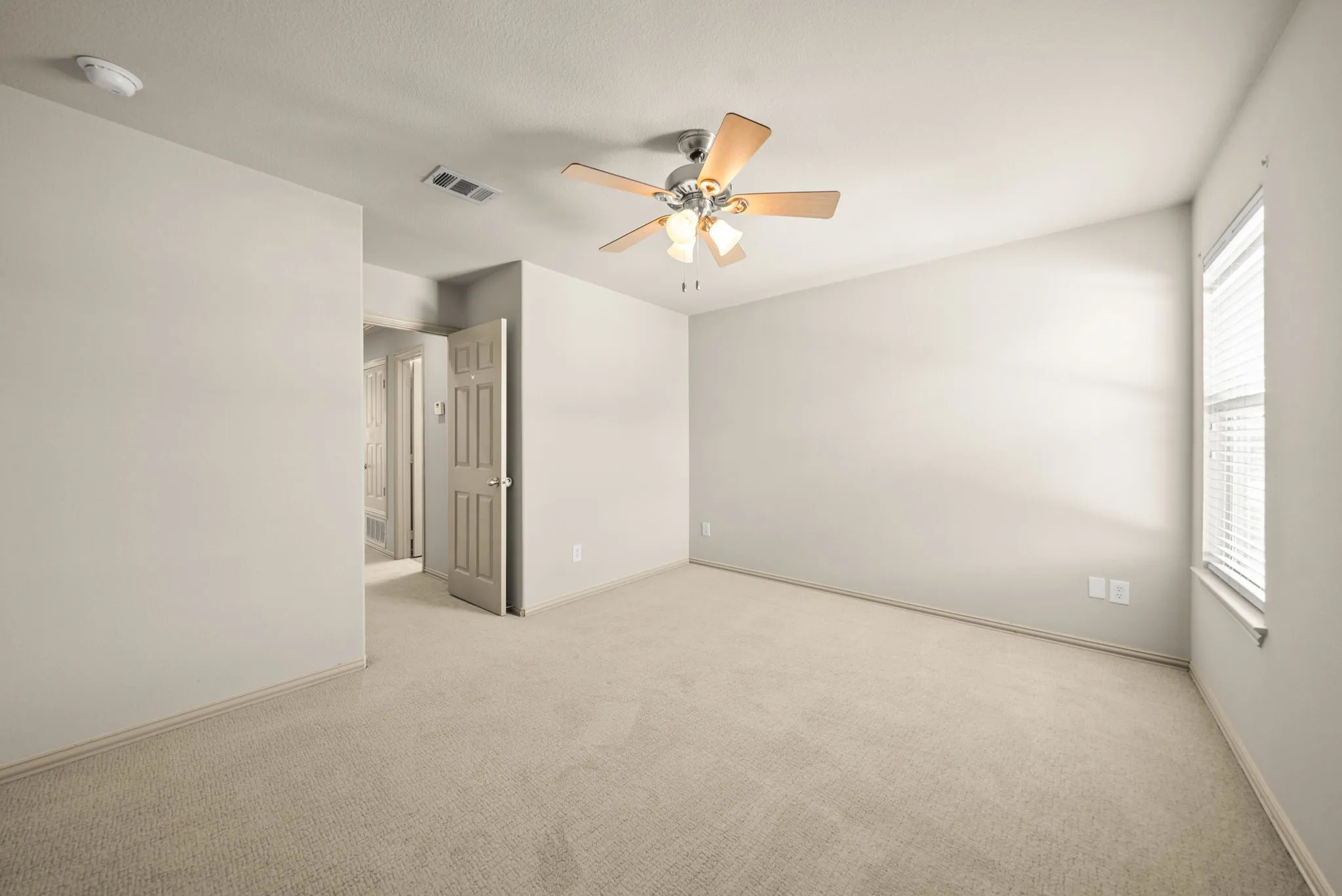 Neutral toned wall paint, plush carpet flooring, ceiling fan with light fixture, window with blinds, and white interior door