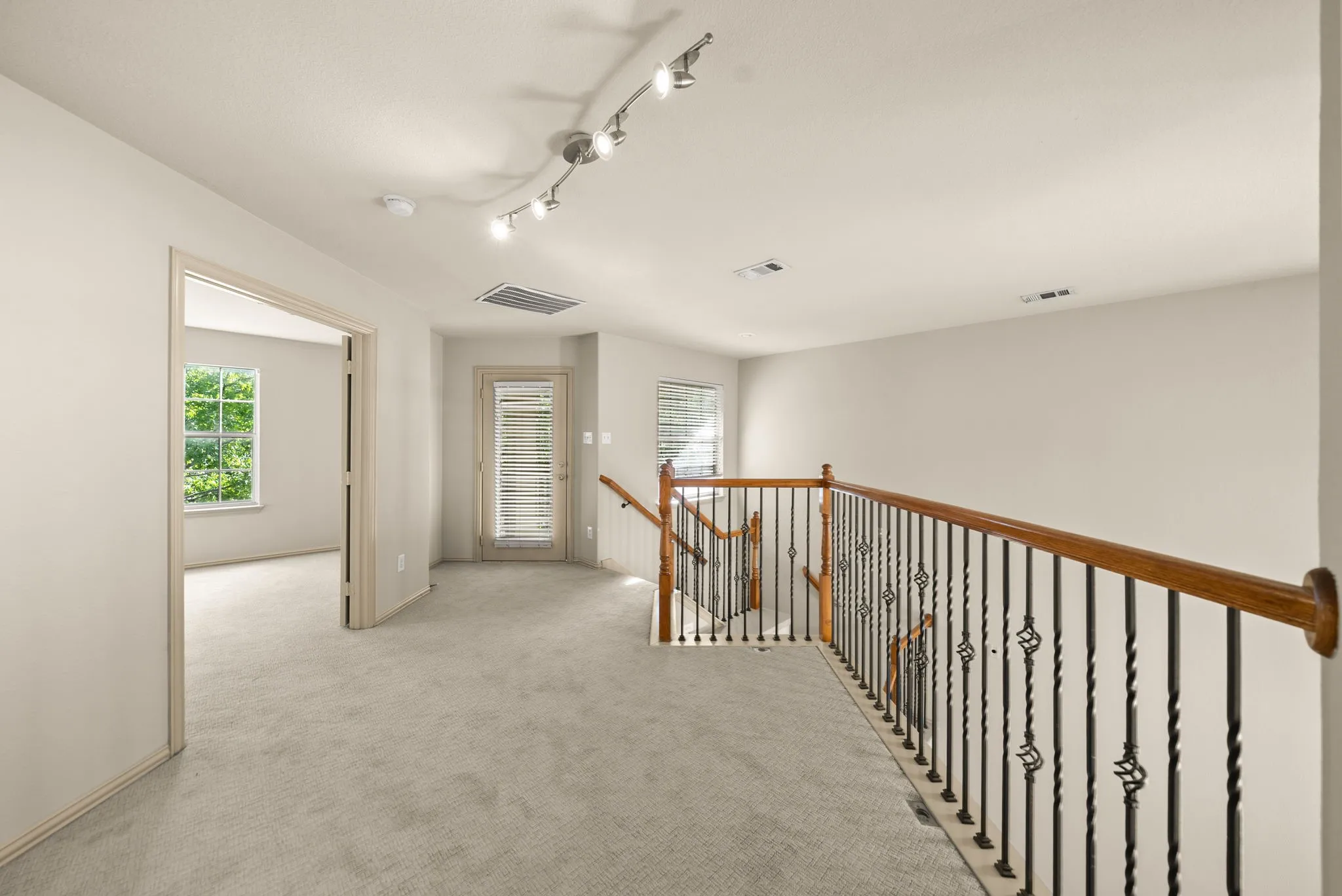 Carpeted landing with wood and wrought iron balustrade, track lighting, and a glass-paneled door