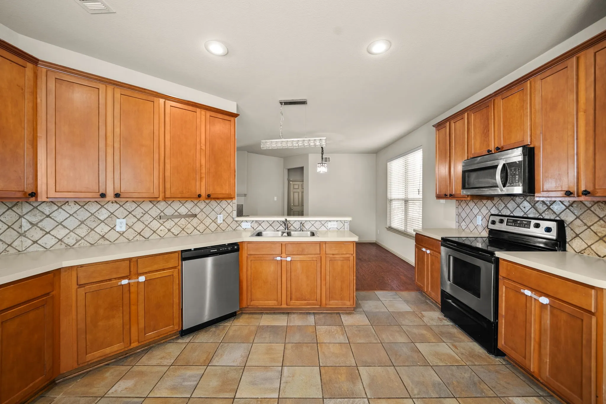 Spacious kitchen featuring warm wood cabinetry, stainless steel appliances including a gas range and microwave, ceramic tile flooring, and a geometric tile backsplash
