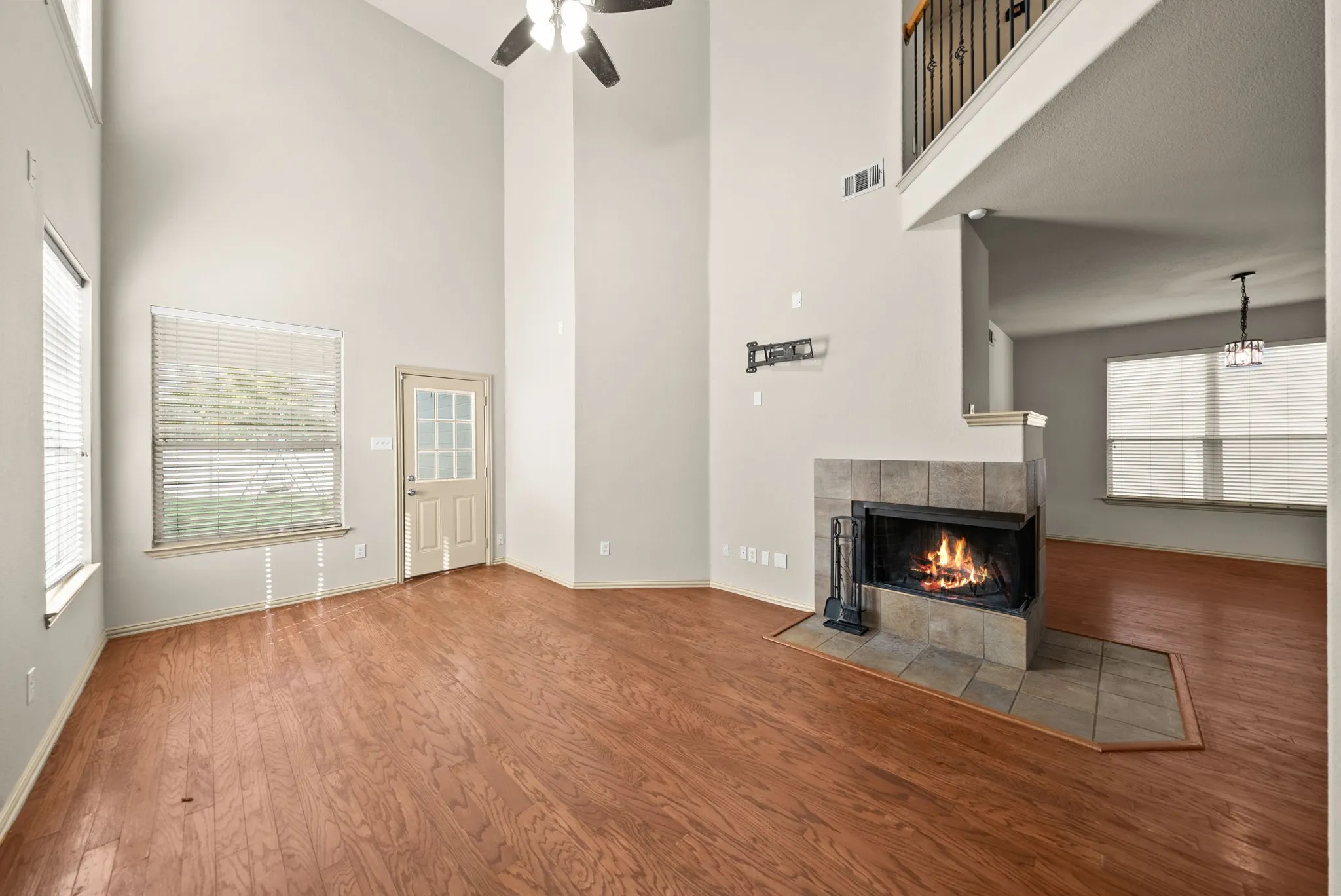 Soaring ceilings with a ceiling fan, wood-finish flooring, tiled fireplace with hearth, and an interior balcony with black wrought iron railing