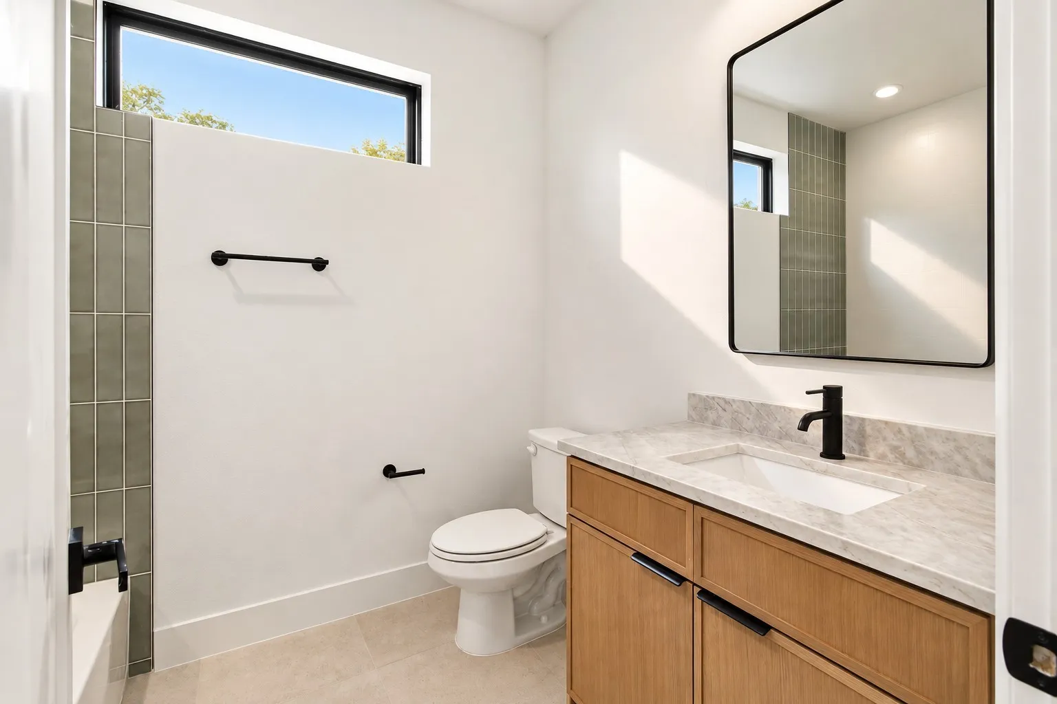 Second Modern bathroom featuring a wood-finish vanity with an integrated sink, stone countertop, matte black fixtures, and a rectangular mirror