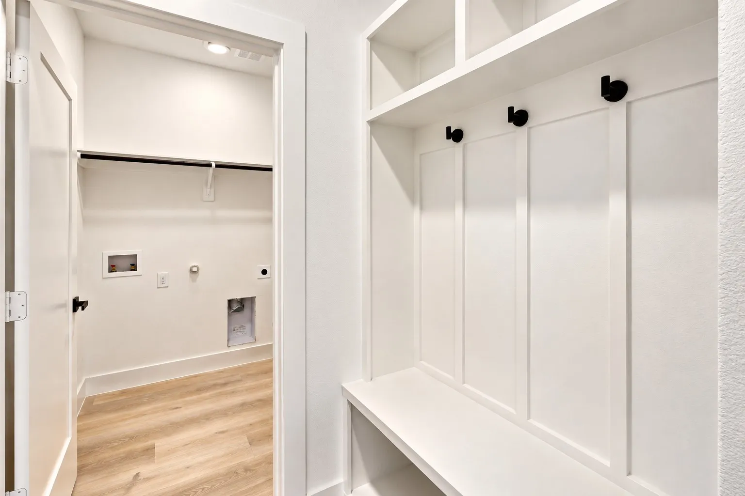 Built-in storage bench with upper shelving, coat hooks, and a laundry room with wood-finish flooring