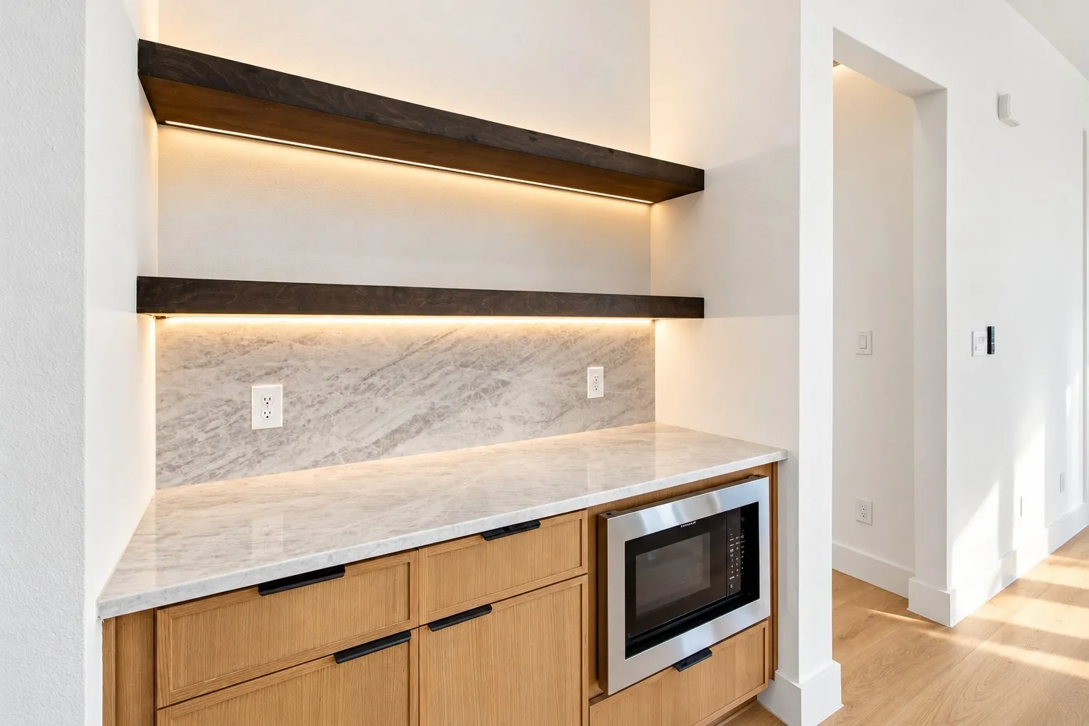 Built-in cabinetry with wood-finish doors, stone countertop, stone backsplash, under-cabinet lighting, and integrated stainless steel microwave