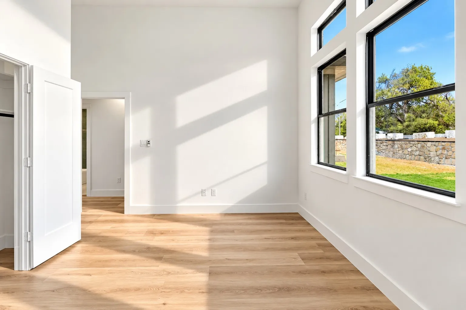 High ceilings, wood-finish flooring, white walls, black-framed windows, and a stone retaining wall