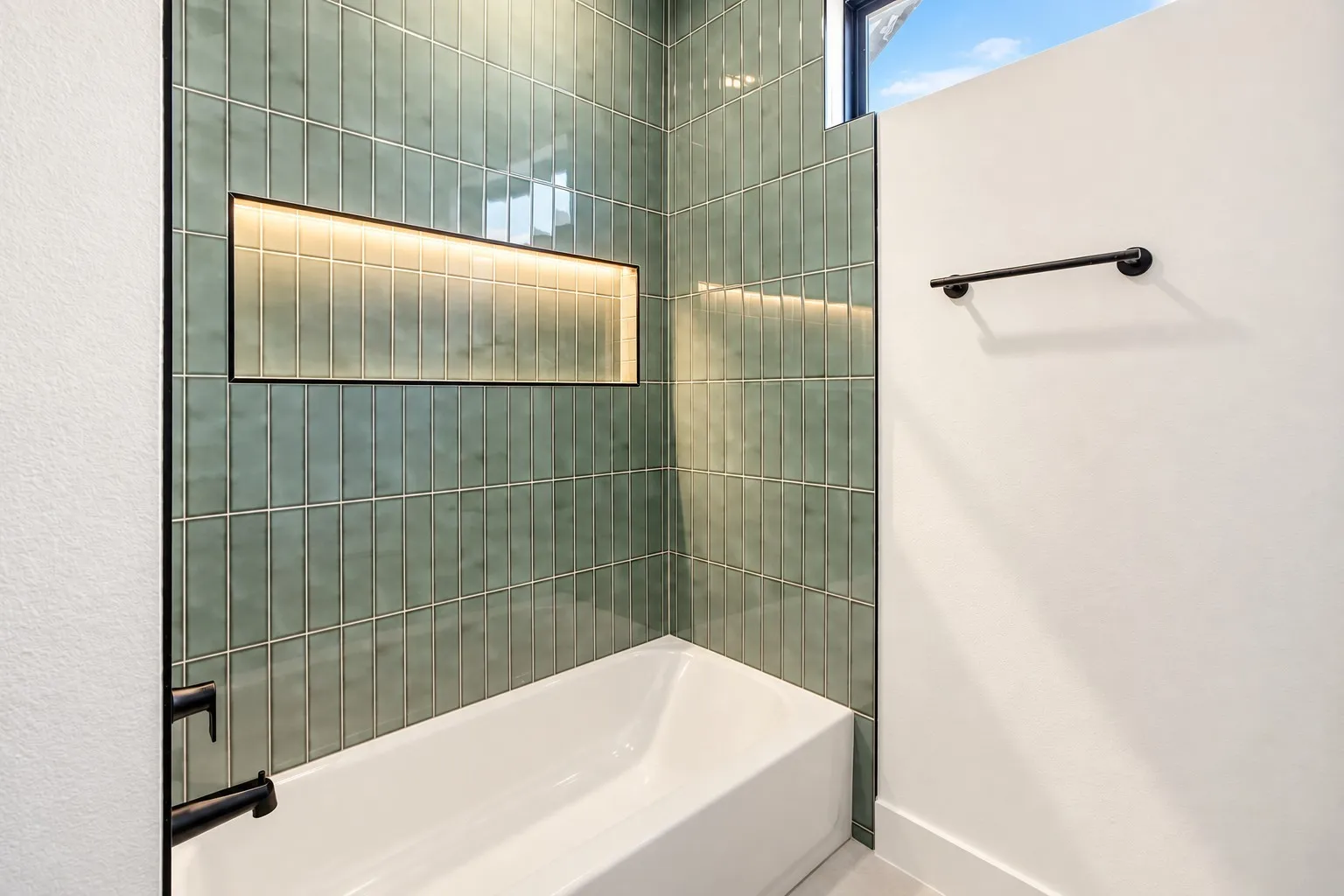 Second Bathtub with contemporary vertical green tile surround, illuminated shower niche, and matte black fixtures