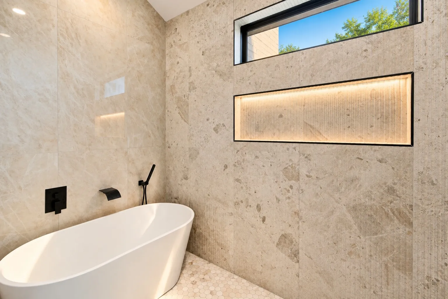 Freestanding soaking tub with matte black fixtures, stone tile walls, illuminated niche, and a horizontal window
