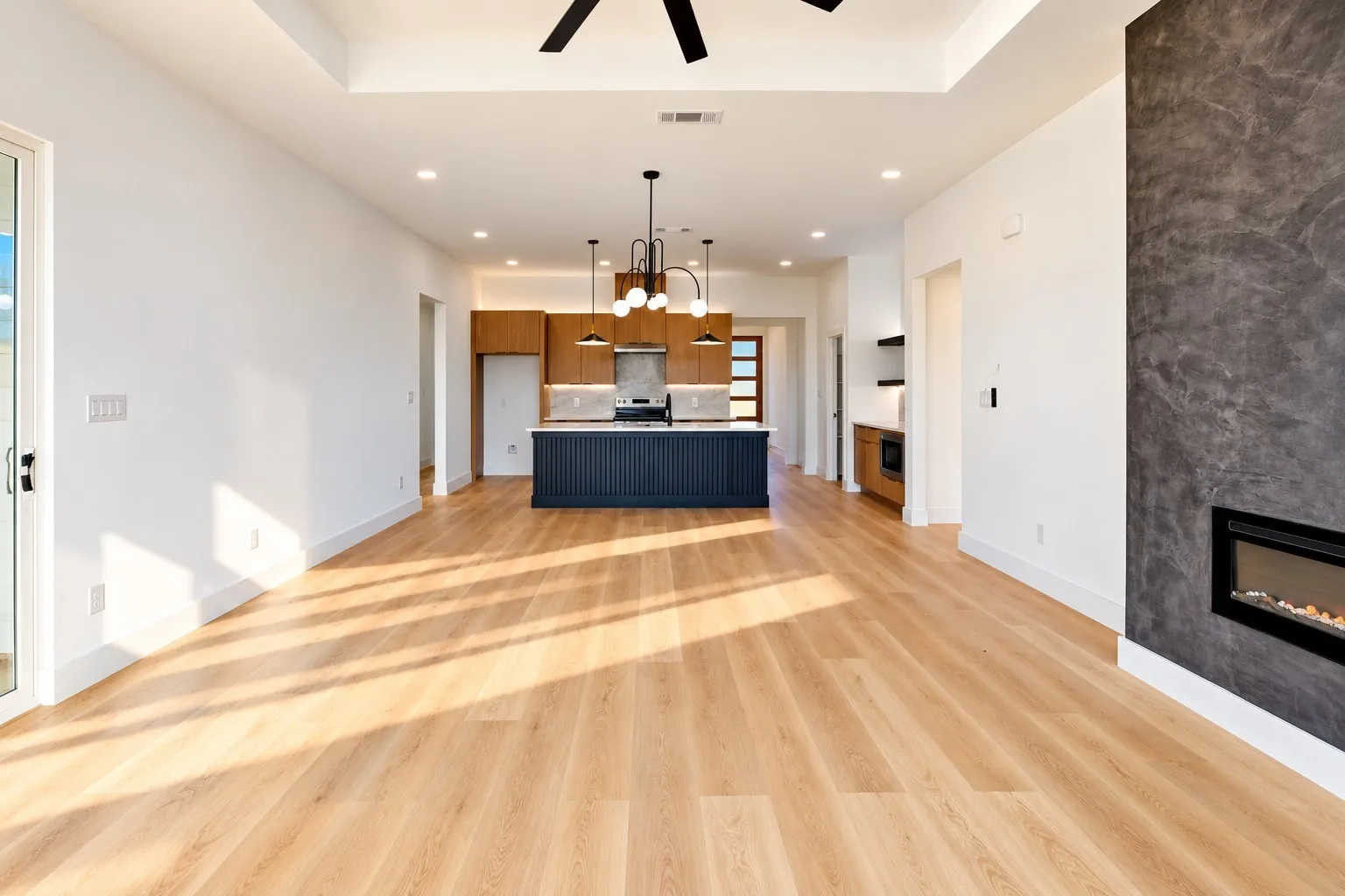 Wood-finish flooring throughout, tray ceiling, recessed lighting, linear electric fireplace, and a kitchen island with pendant lighting