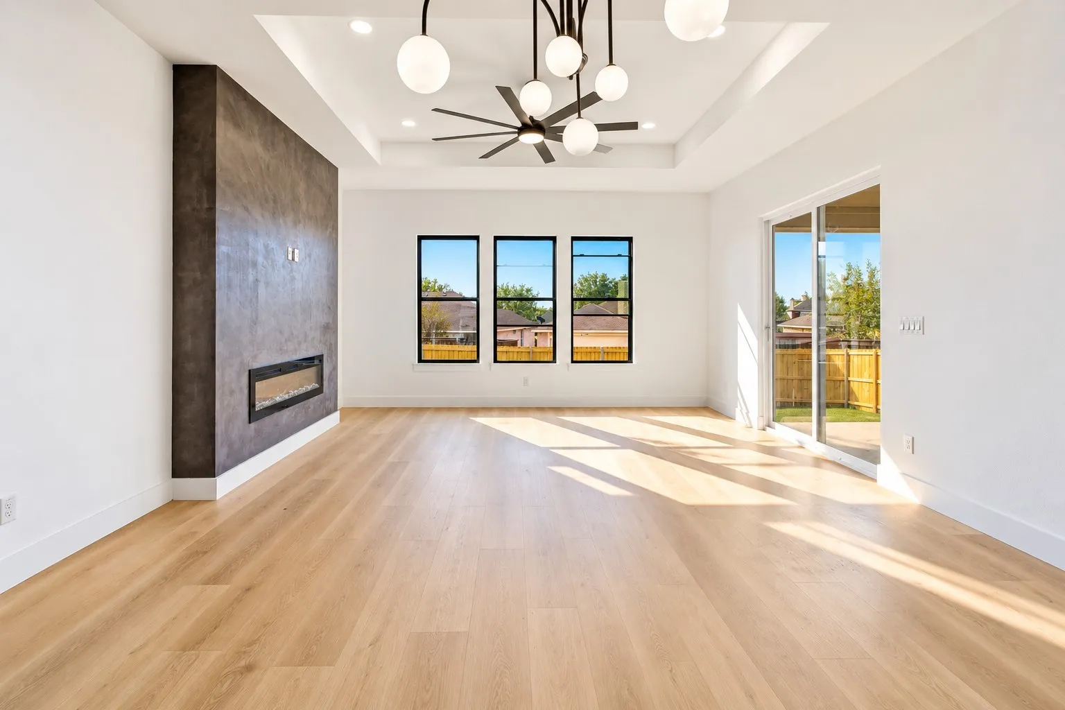 Tray ceiling with recessed lighting and contemporary chandelier, wood-finish flooring, linear electric fireplace, three large windows, and sliding glass door