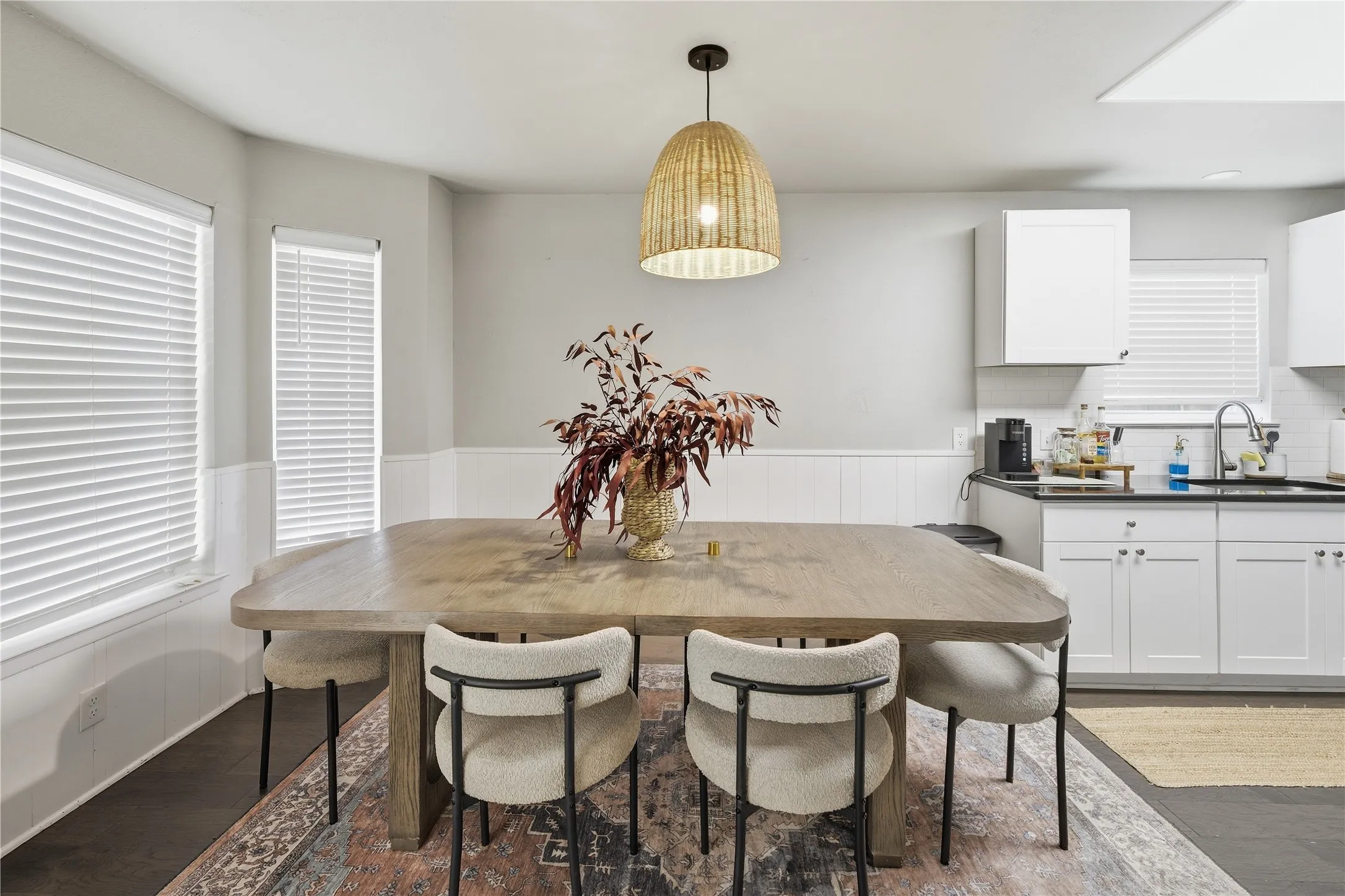 Dining area featuring a woven pendant light fixture, white wainscoting, and wood-finish flooring