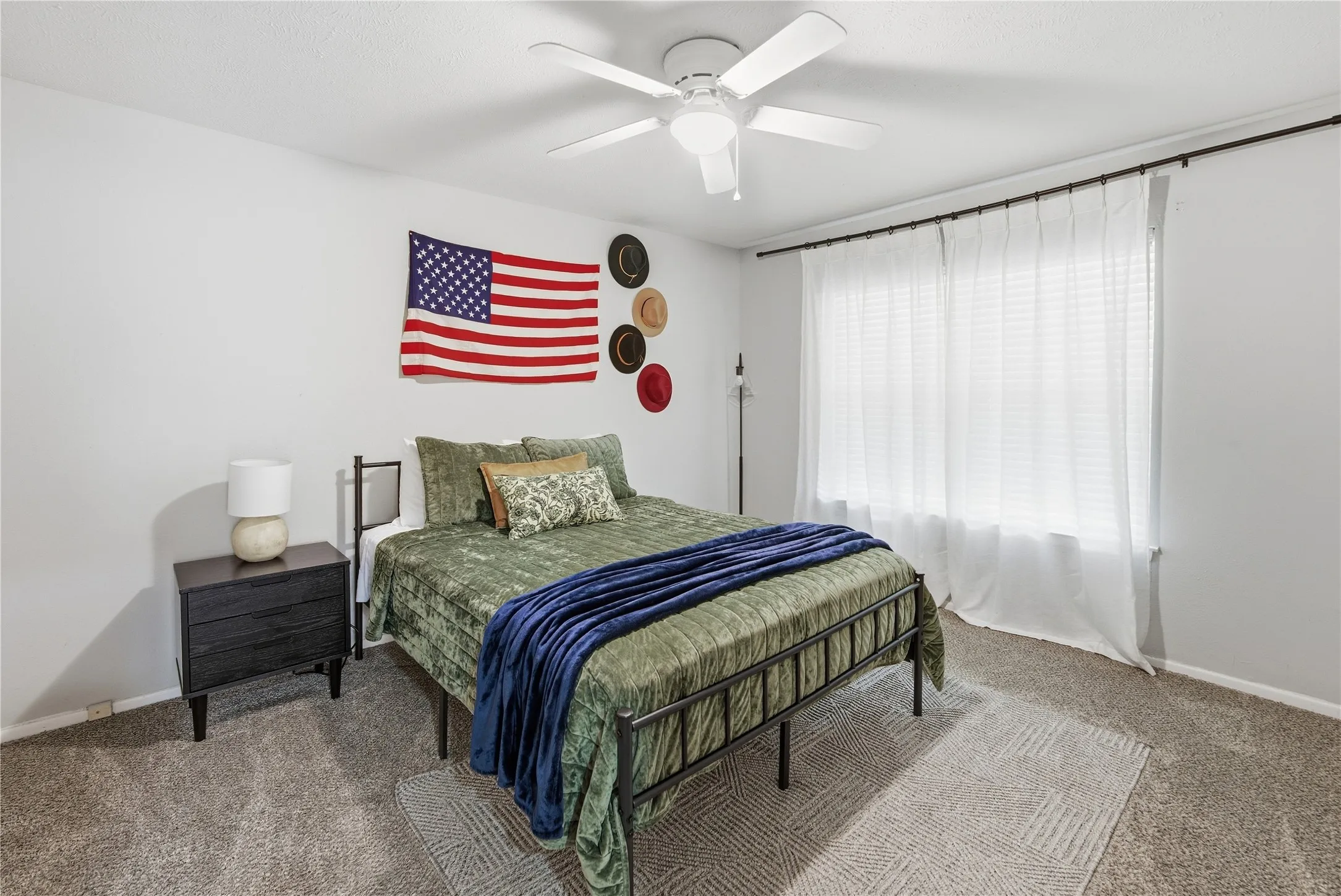 Recessed window with white curtains, neutral tone carpet flooring, white painted walls, and a ceiling fan