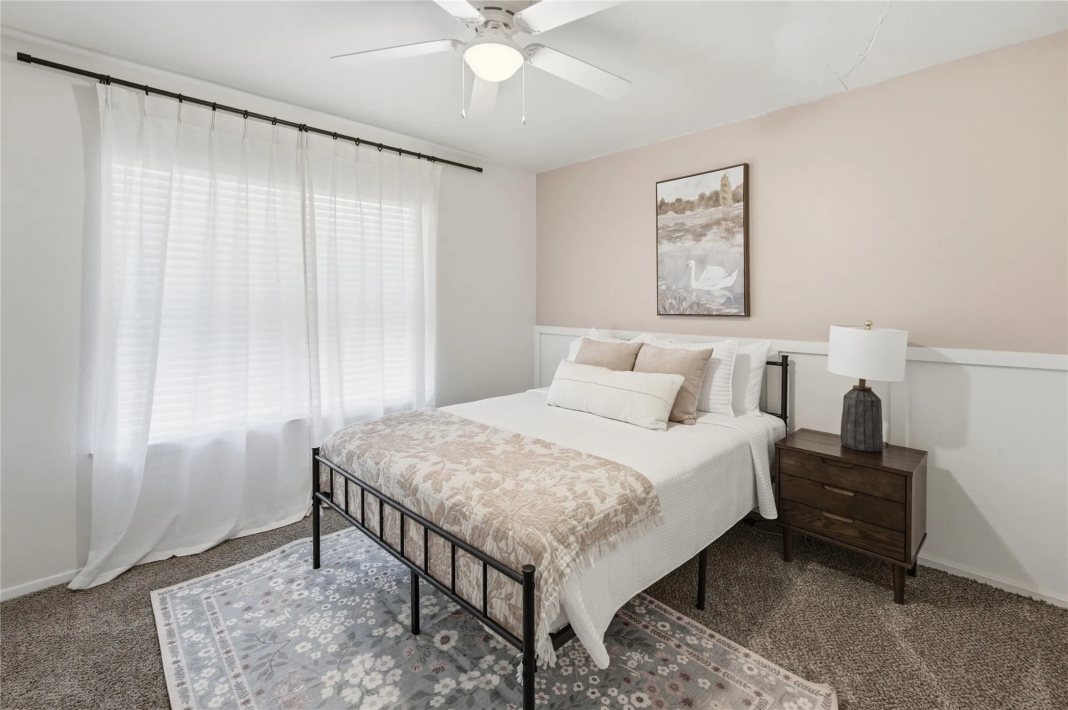 Built-in ceiling fan with light fixture, window with privacy blinds and sheer curtains, wainscoting detail, and carpeted flooring