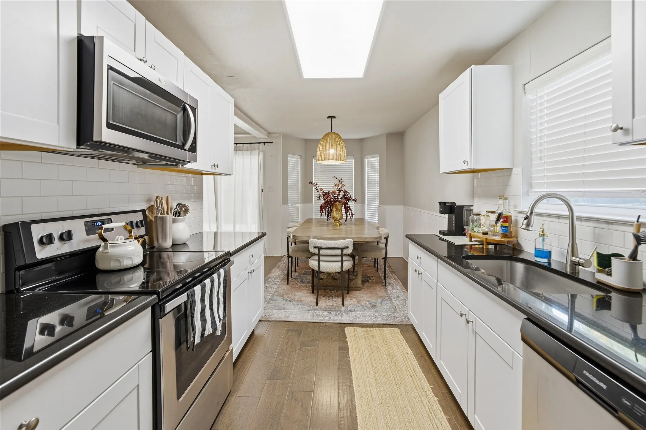 White cabinetry with black countertops, stainless steel appliances, and a subway tile backsplash