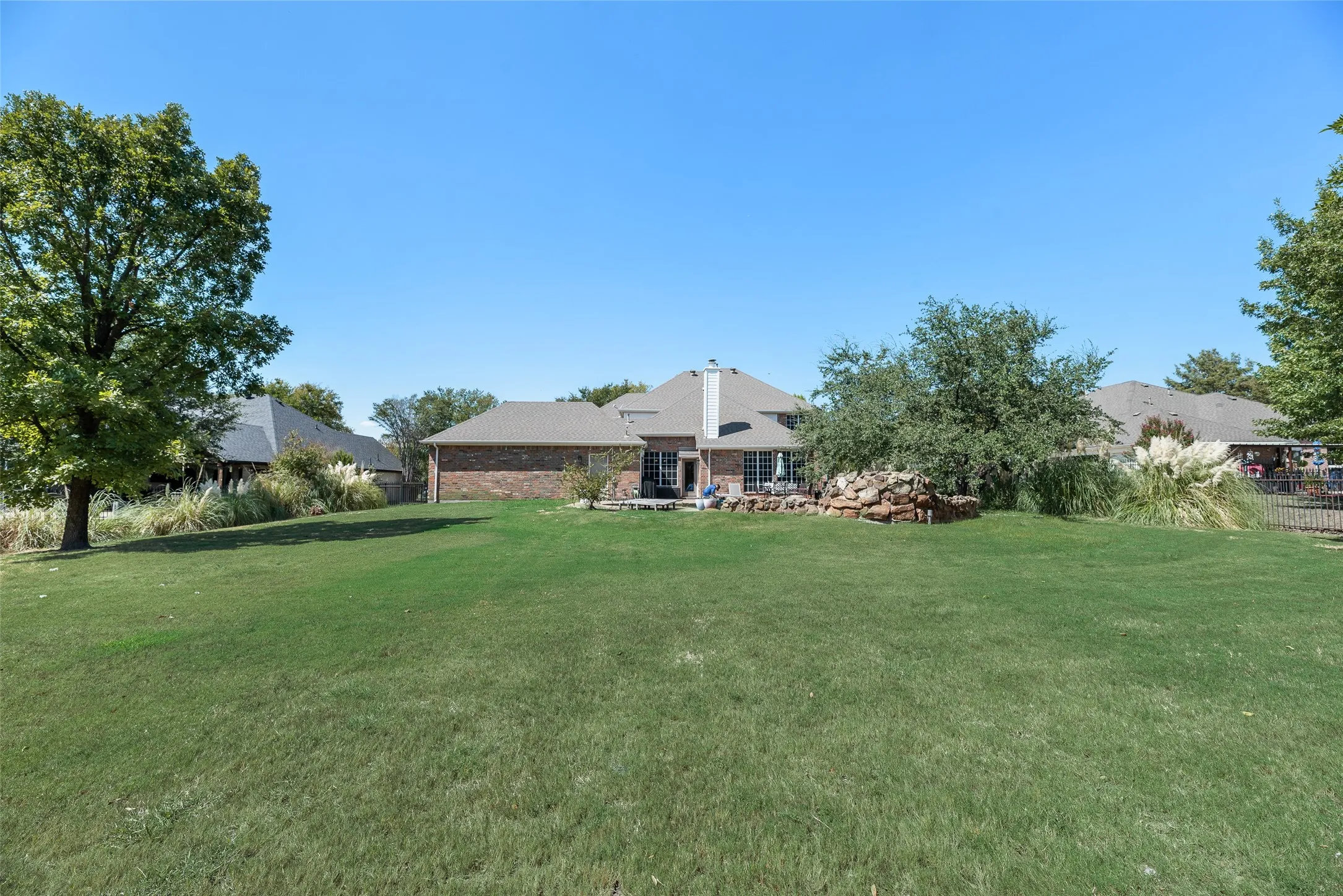 Expansive green lawn with mature trees and a brick exterior residence featuring a patio area