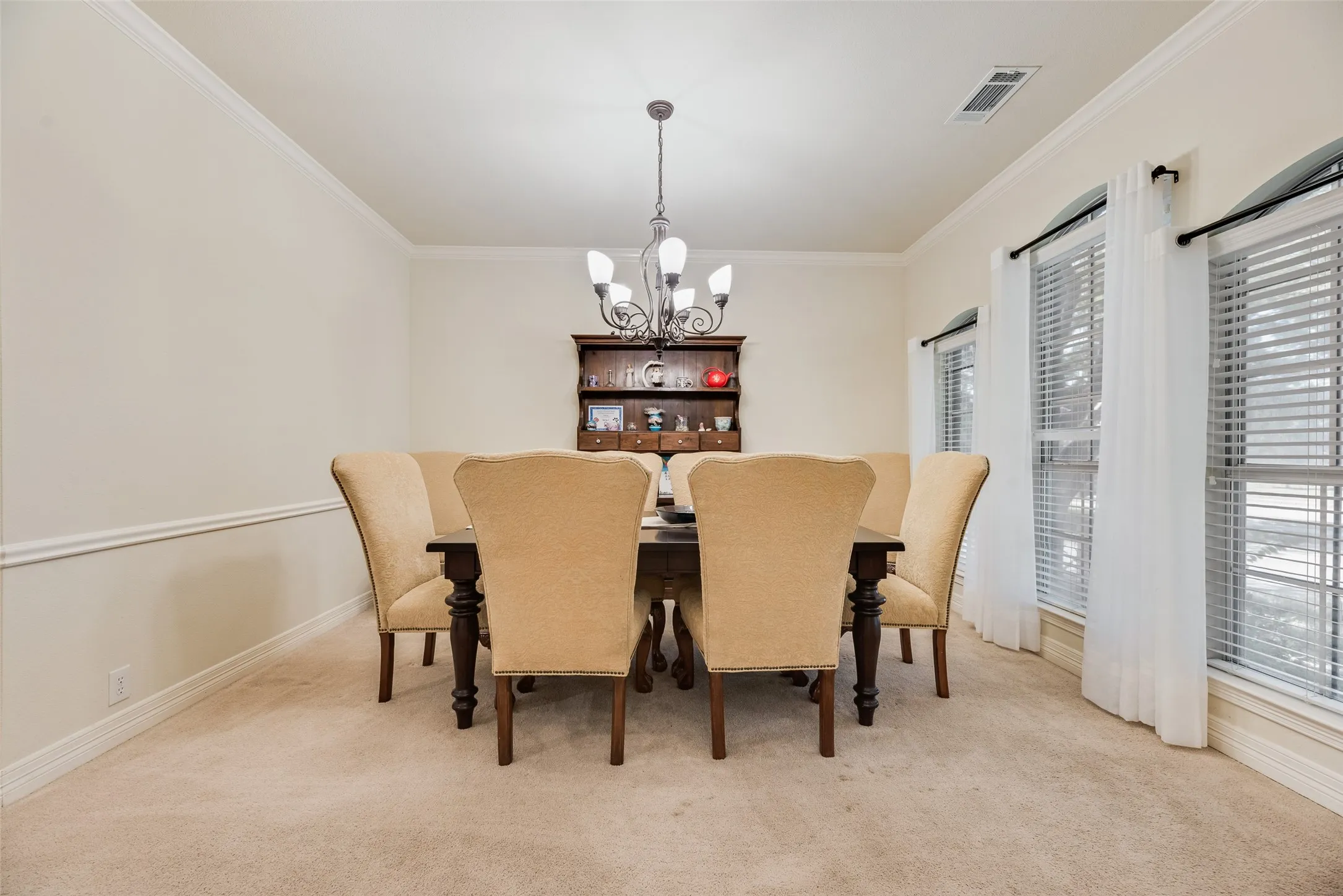 Formal dining room showcasing elegant pendant lighting, neutral wall finishes with chair rail molding, and expansive windows with plantation shutters
