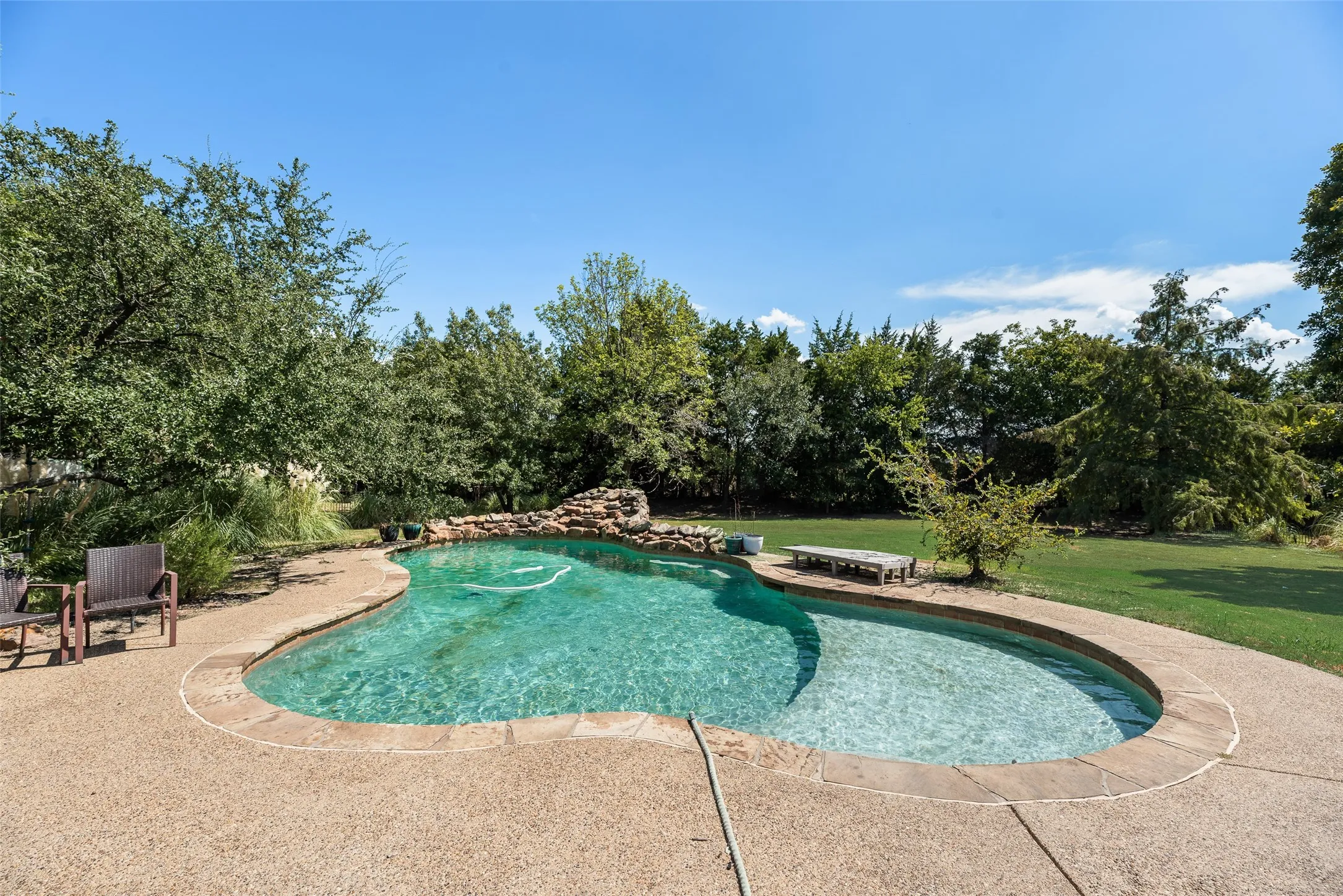 Freeform swimming pool with a rock waterfall feature, integrated spa, and concrete decking