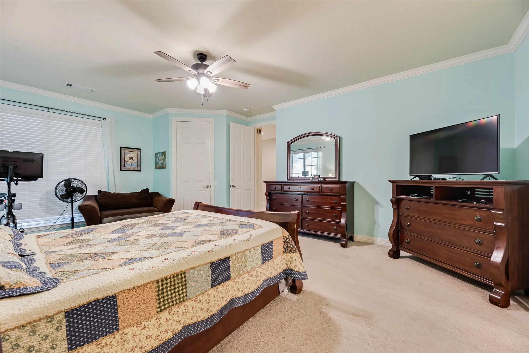 Recessed ceiling with a ceiling fan, white crown molding, light blue walls, and a large window with blinds