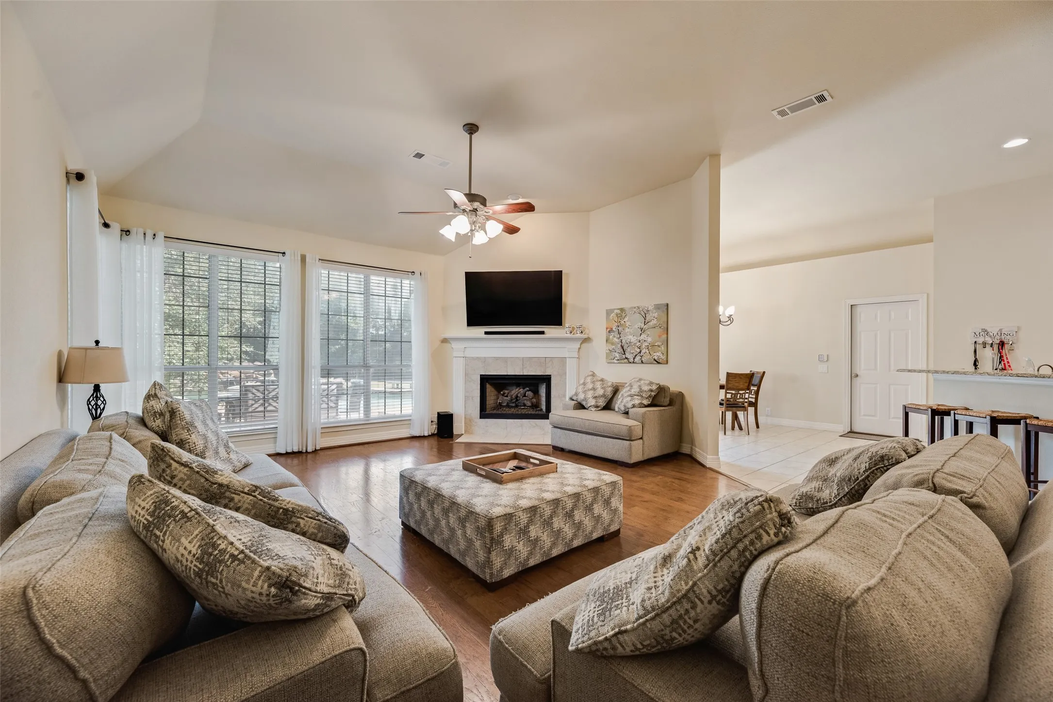 Spacious living area featuring expansive windows, wood-finish flooring, a ceiling fan, and a fireplace with a mantel
