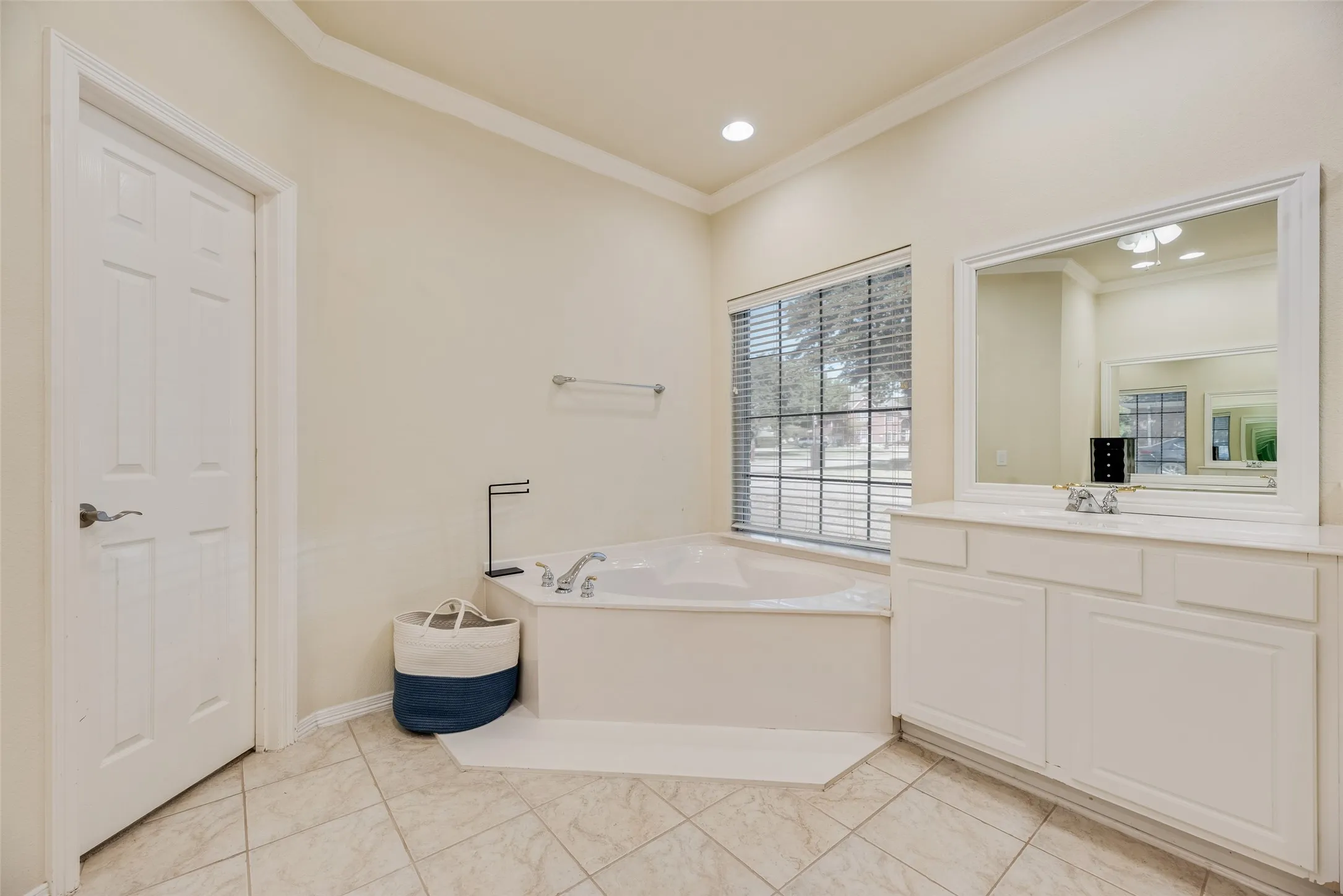 Corner soaking tub with a large window, tiled flooring, built-in vanity with integrated sink, and an expansive mirror