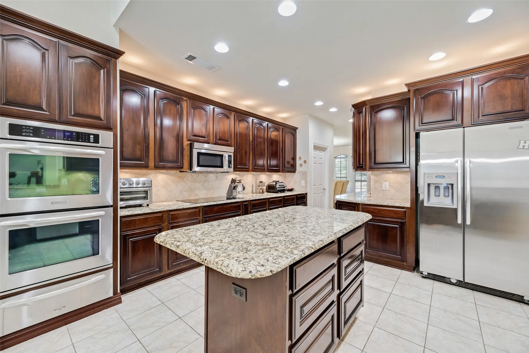 Kitchen featuring dark wood cabinetry, light granite countertops, stainless steel appliances, and recessed lighting