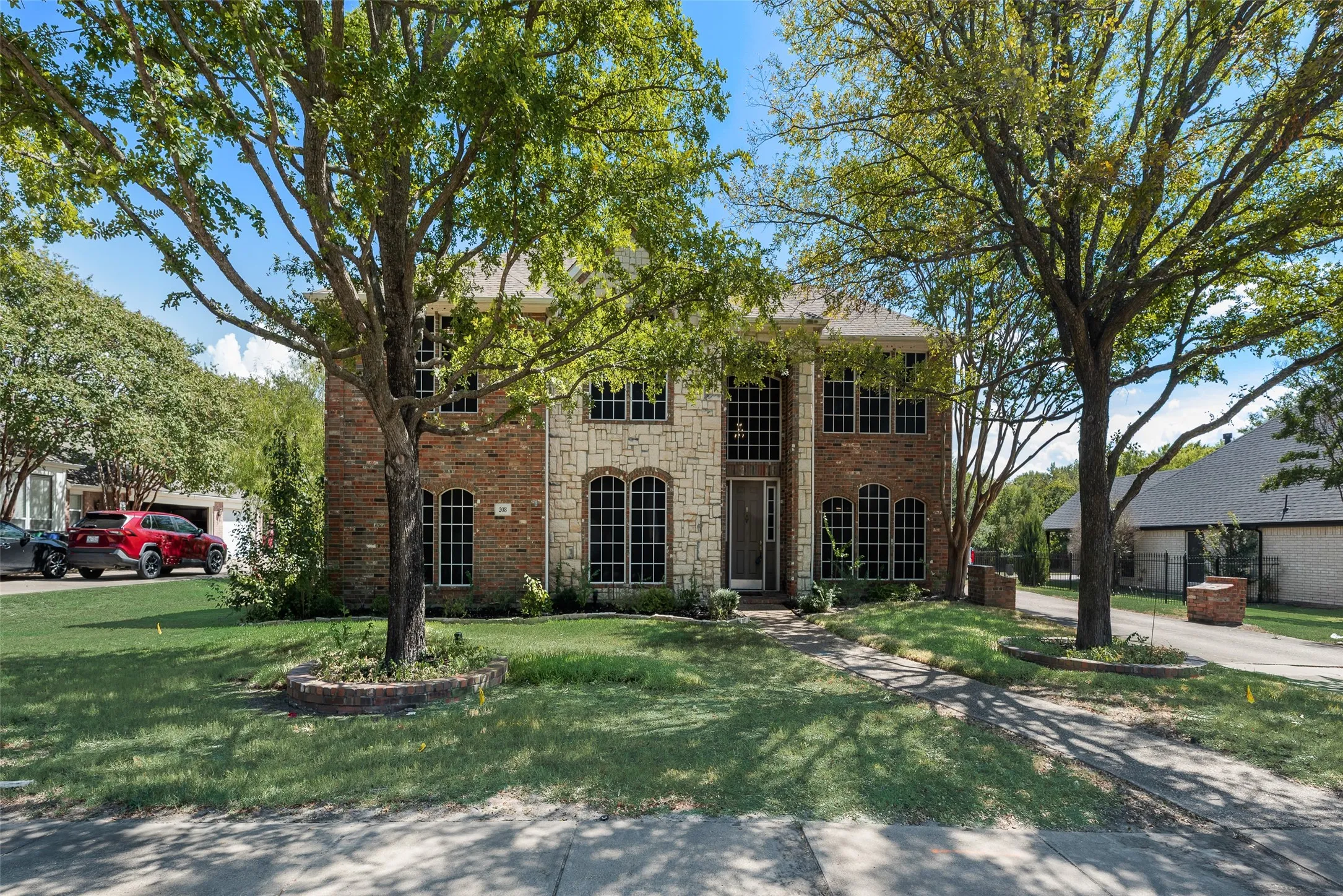 Two-story residence featuring a brick and stone facade, arched windows, and mature trees framing the entry