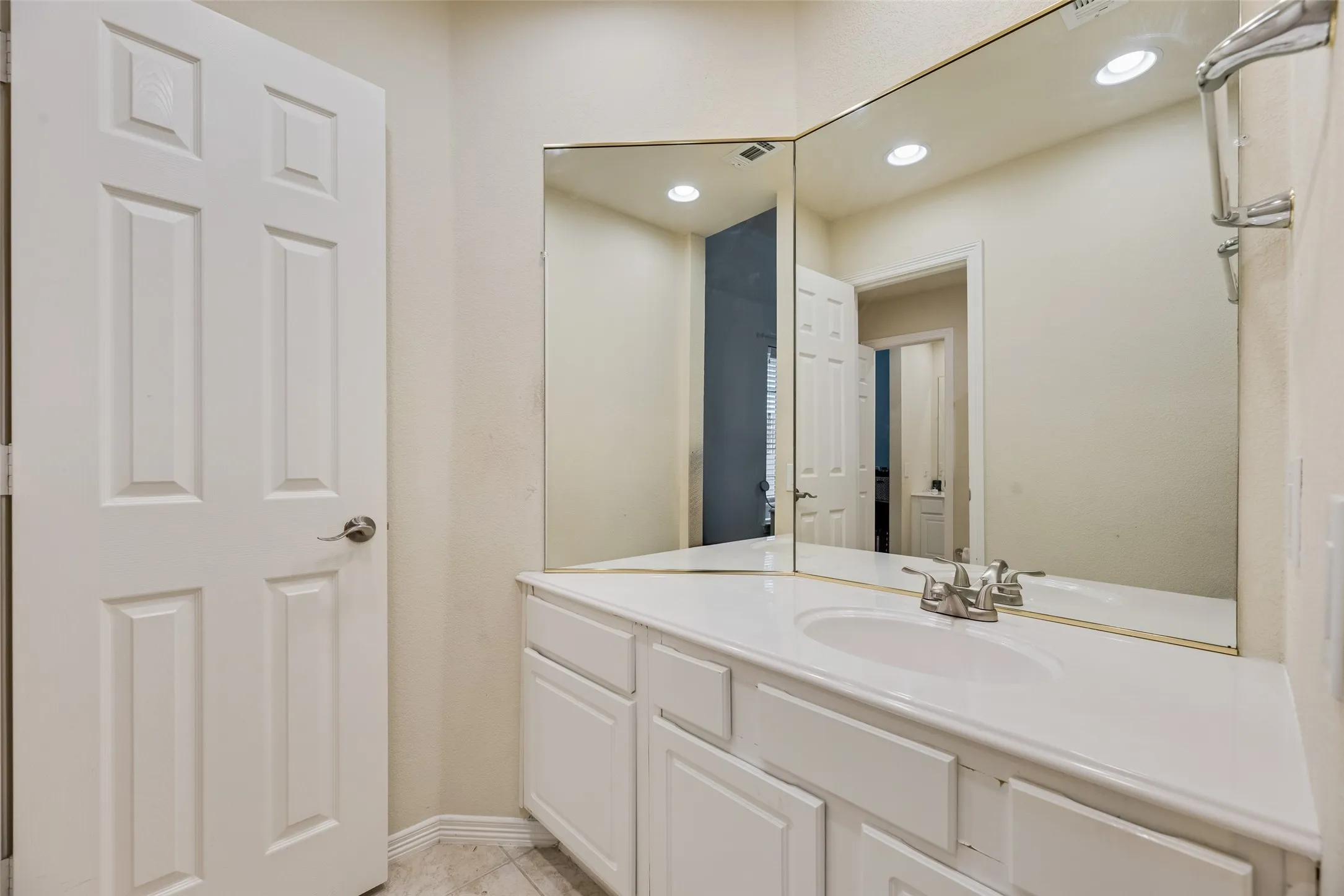 White paneled door, integrated vanity with a single basin sink, brushed nickel faucet, large wall-mounted mirror, and recessed lighting