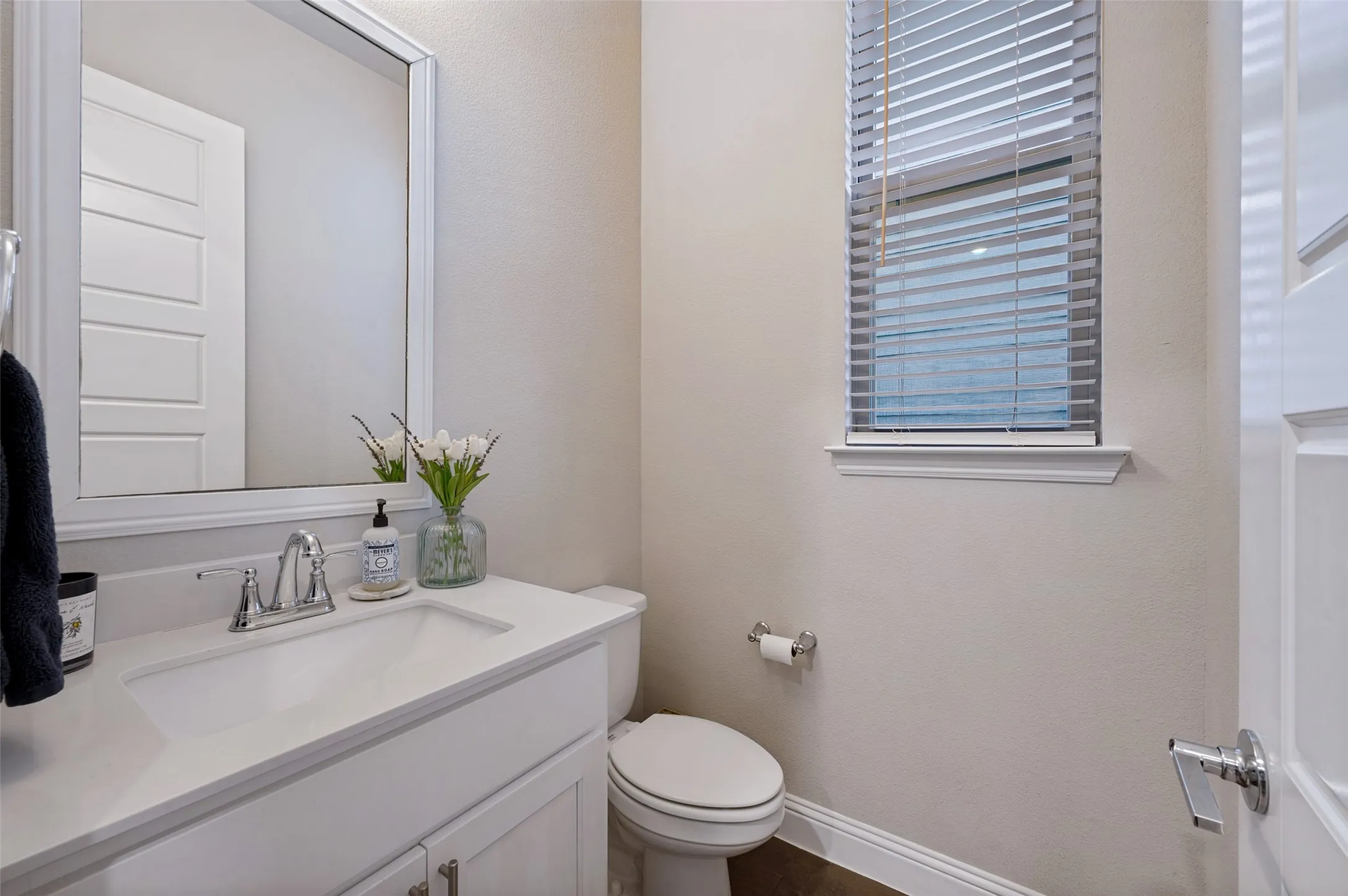 White vanity with integrated sink, chrome faucet, framed mirror, and window with blinds