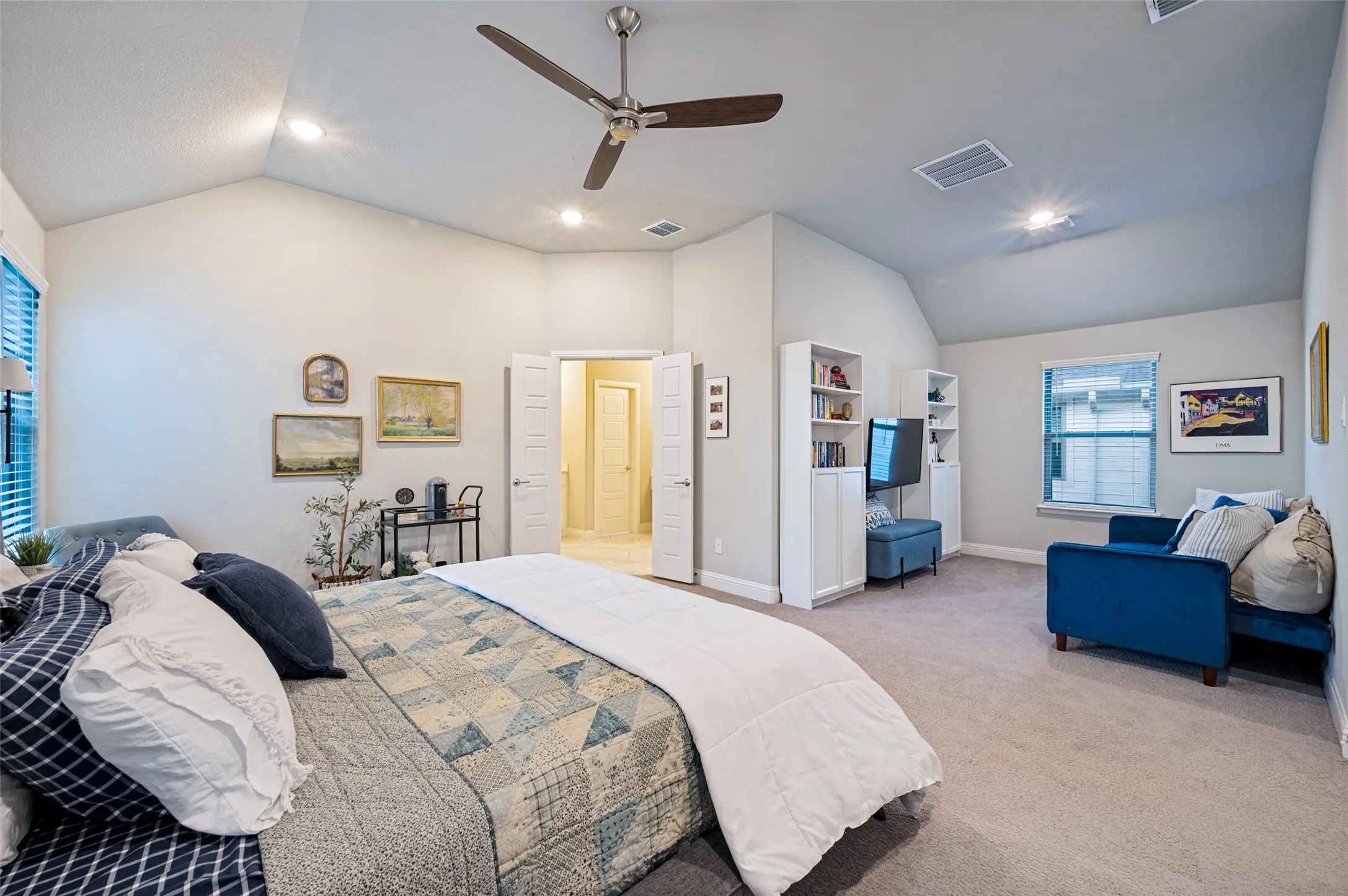 Primary bedroom and seating area feature vaulted ceilings with recessed lighting and a ceiling fan, carpet flooring, window with blinds.