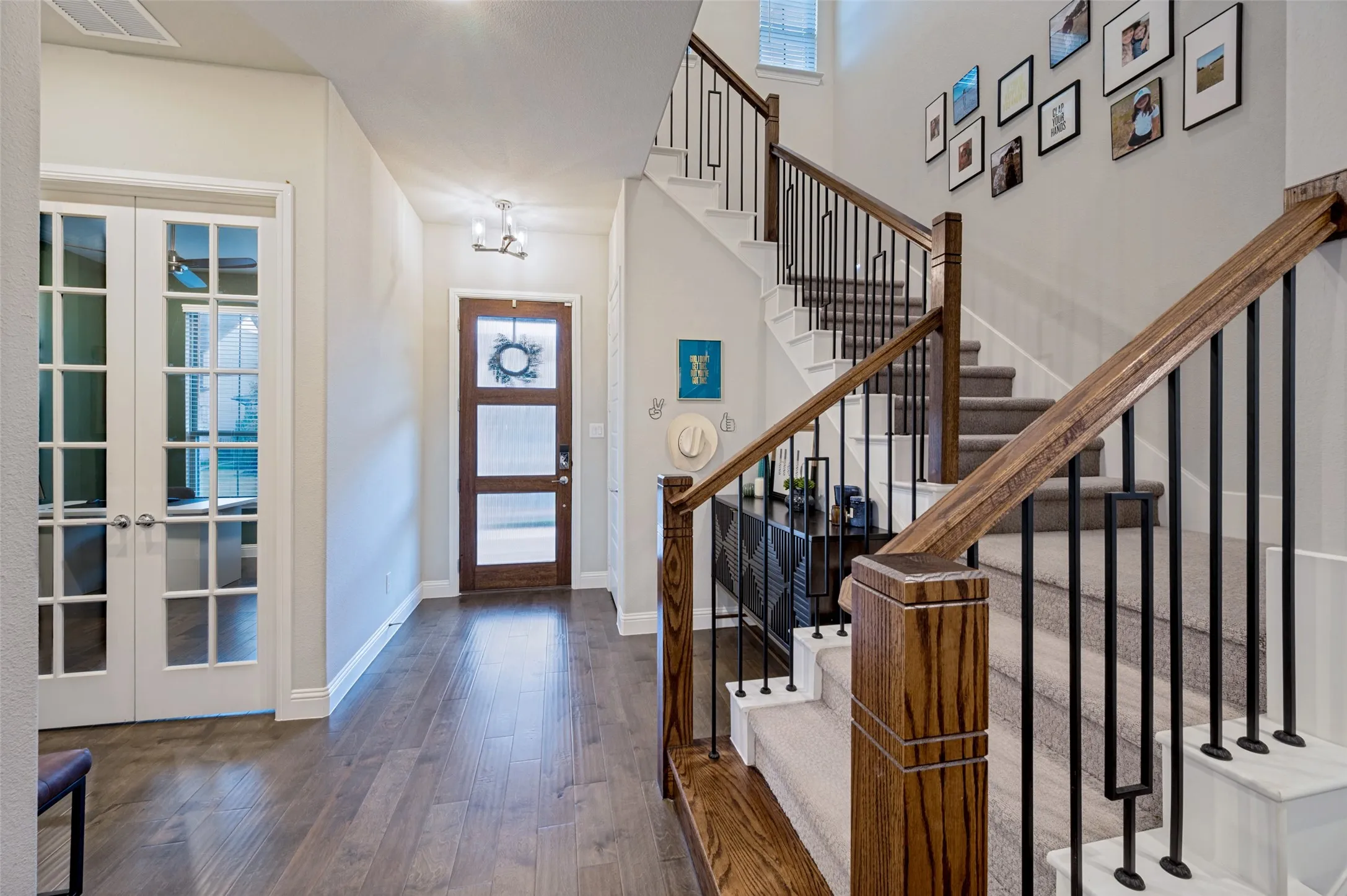 Wood-finish flooring, staircase with carpeted treads, wood handrails with black metal balusters, and a solid wood entry door with frosted glass panels