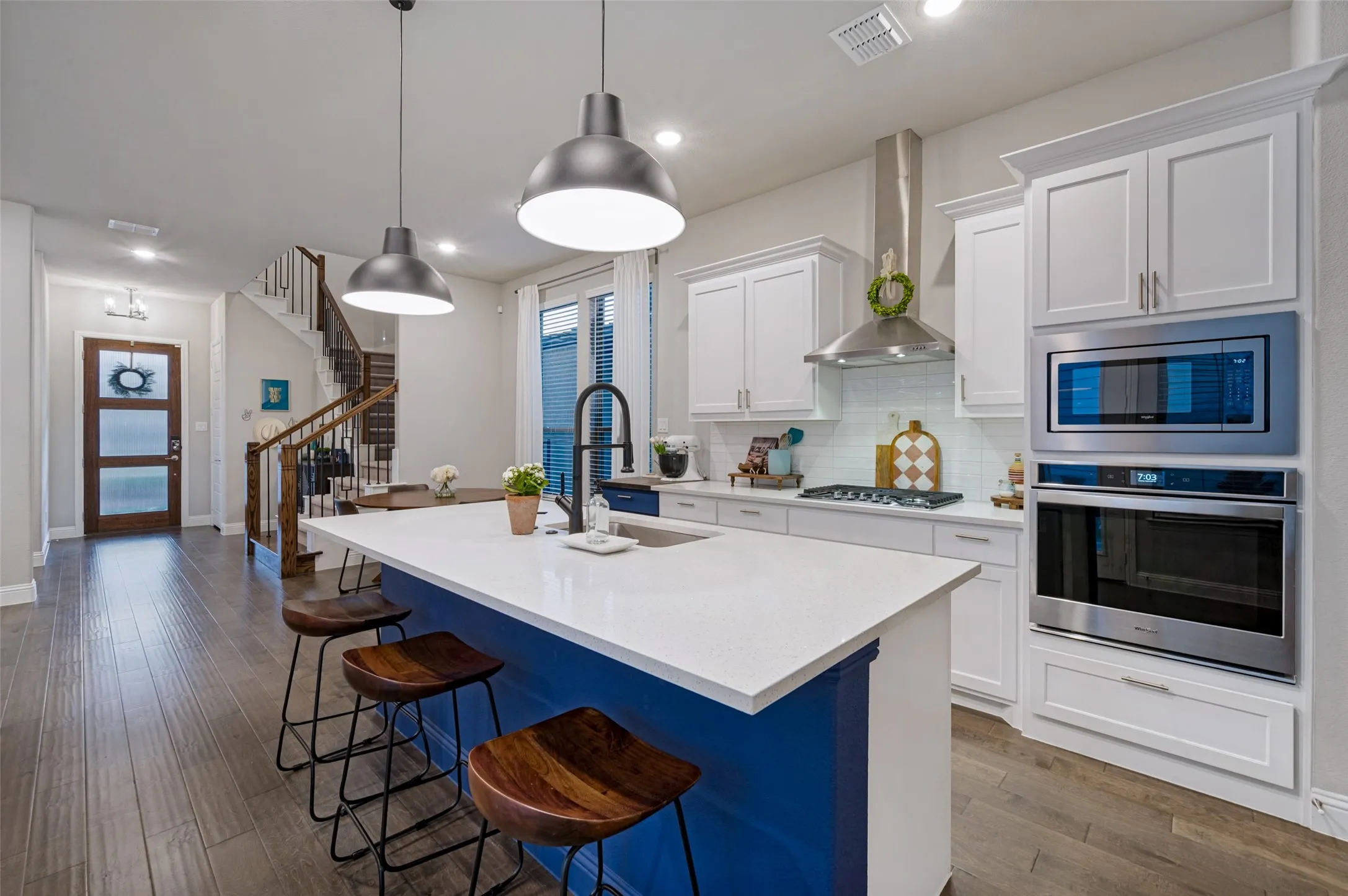 Open-concept kitchen with a white countertop island, stainless steel appliances, white cabinetry, and wood-finish flooring