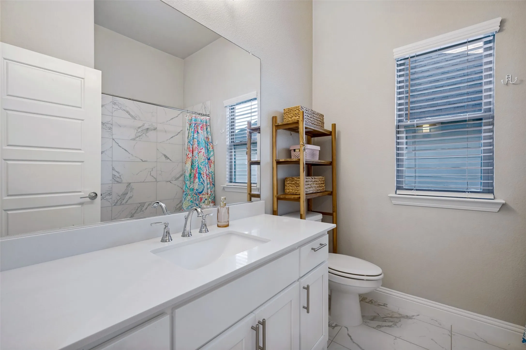 White vanity with an integrated sink, polished chrome faucet, full-width mirror, and white tile flooring