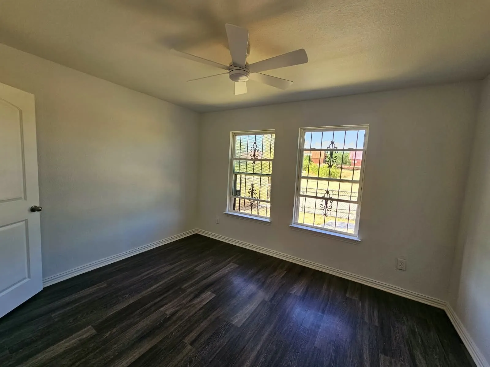 Wood-finish flooring, dual windows with decorative security bars, and a ceiling fan