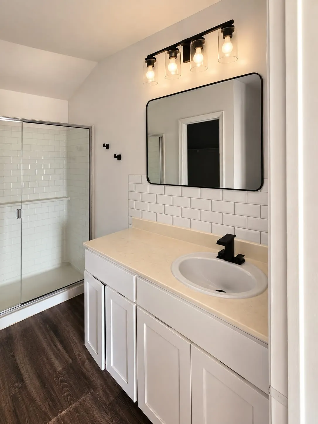 Shower with sliding glass enclosure, white subway tile surround, vanity with white shaker-style cabinetry, and a black-framed rectangular mirror