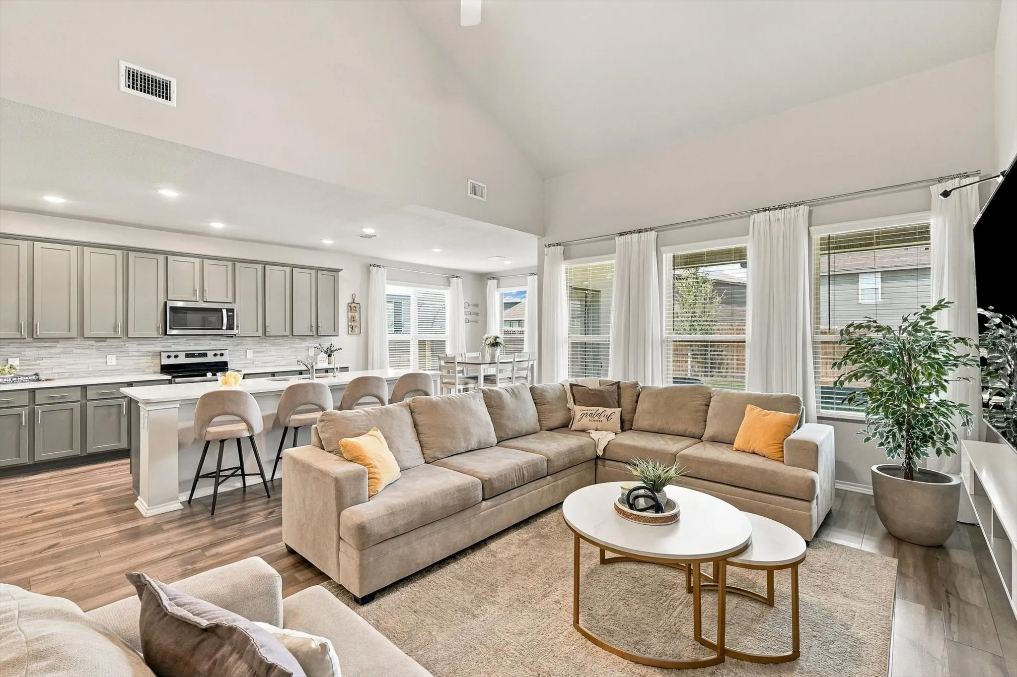 Vaulted ceiling, open-concept living space, wood-finish flooring, island with breakfast bar seating, and stainless steel appliances