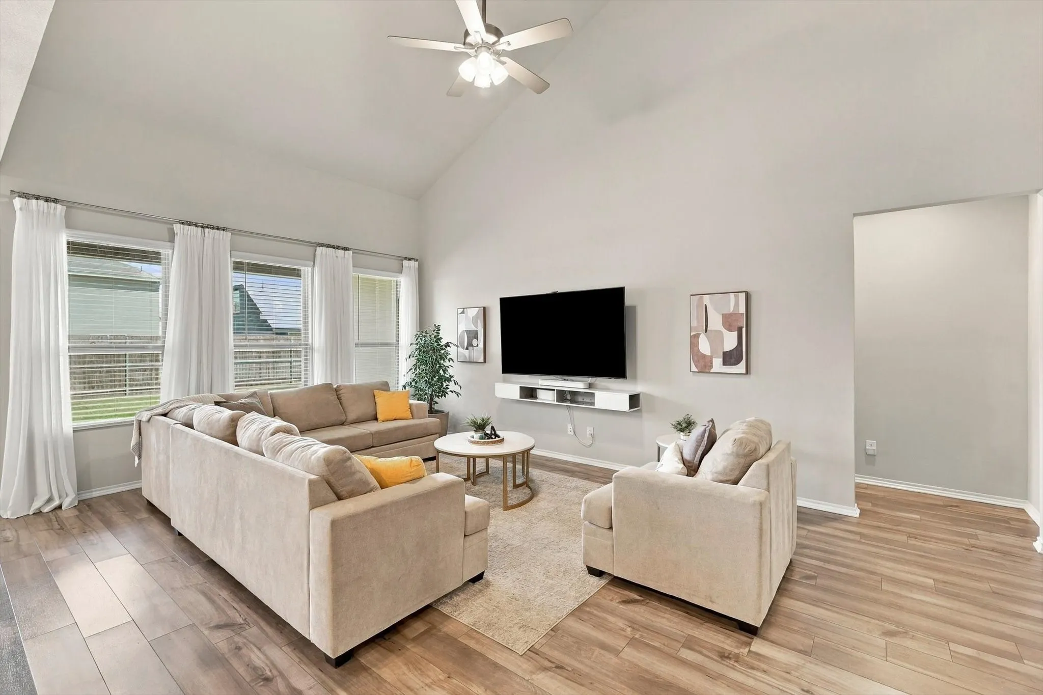 Vaulted ceiling, ceiling fan, wood-finish flooring, multiple windows, wall-mounted media console