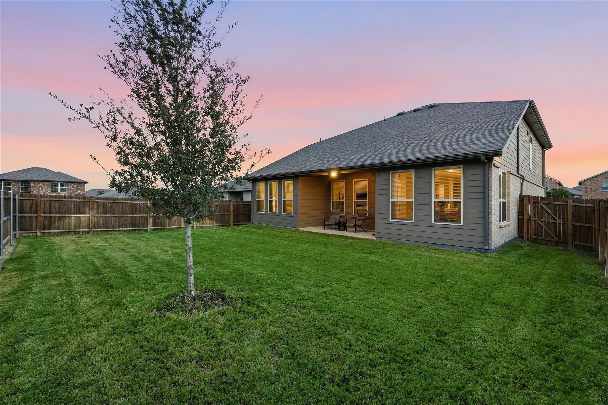 Expansive backyard with a manicured lawn, established tree, and wood privacy fencing